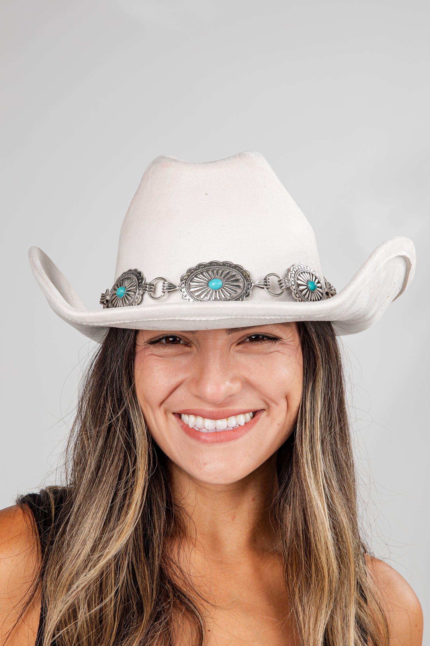Woman wearing a white cowboy hat with decorative band against a gray background