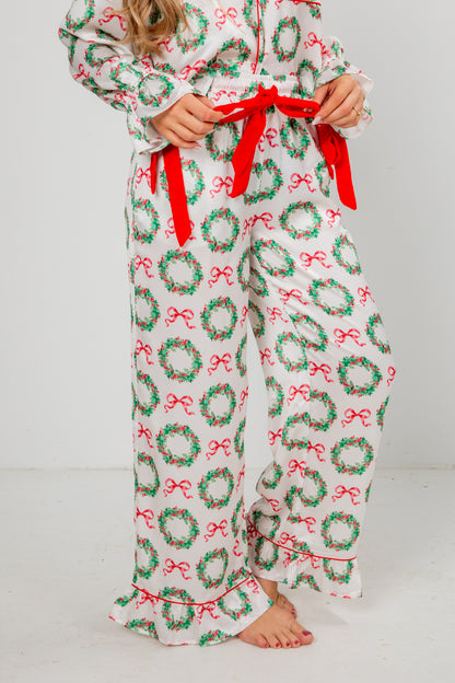 Person wearing a festive pajama set with wreath and bow pattern on a plain background