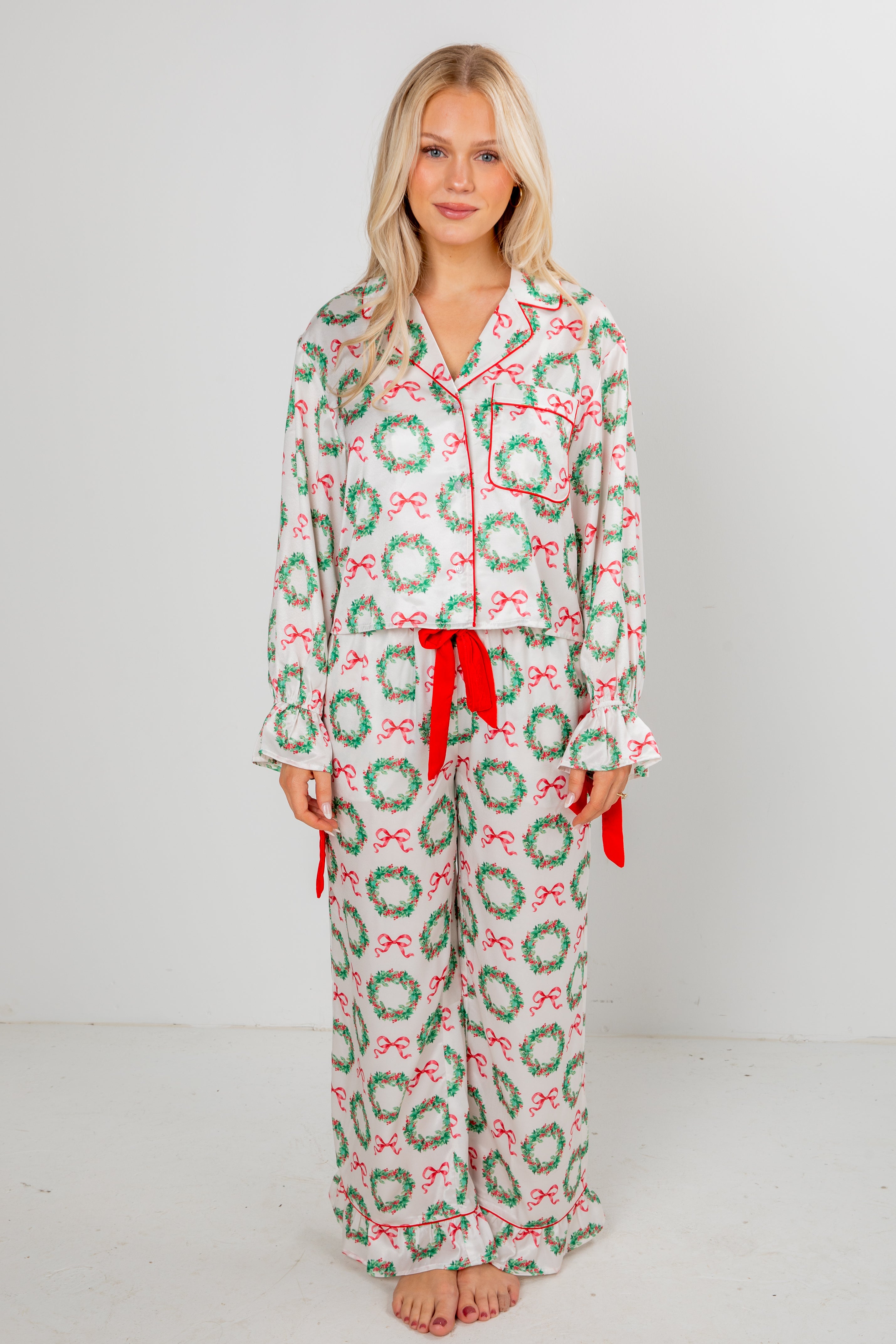Woman wearing a festive pajama set with wreath and bow pattern on a plain background