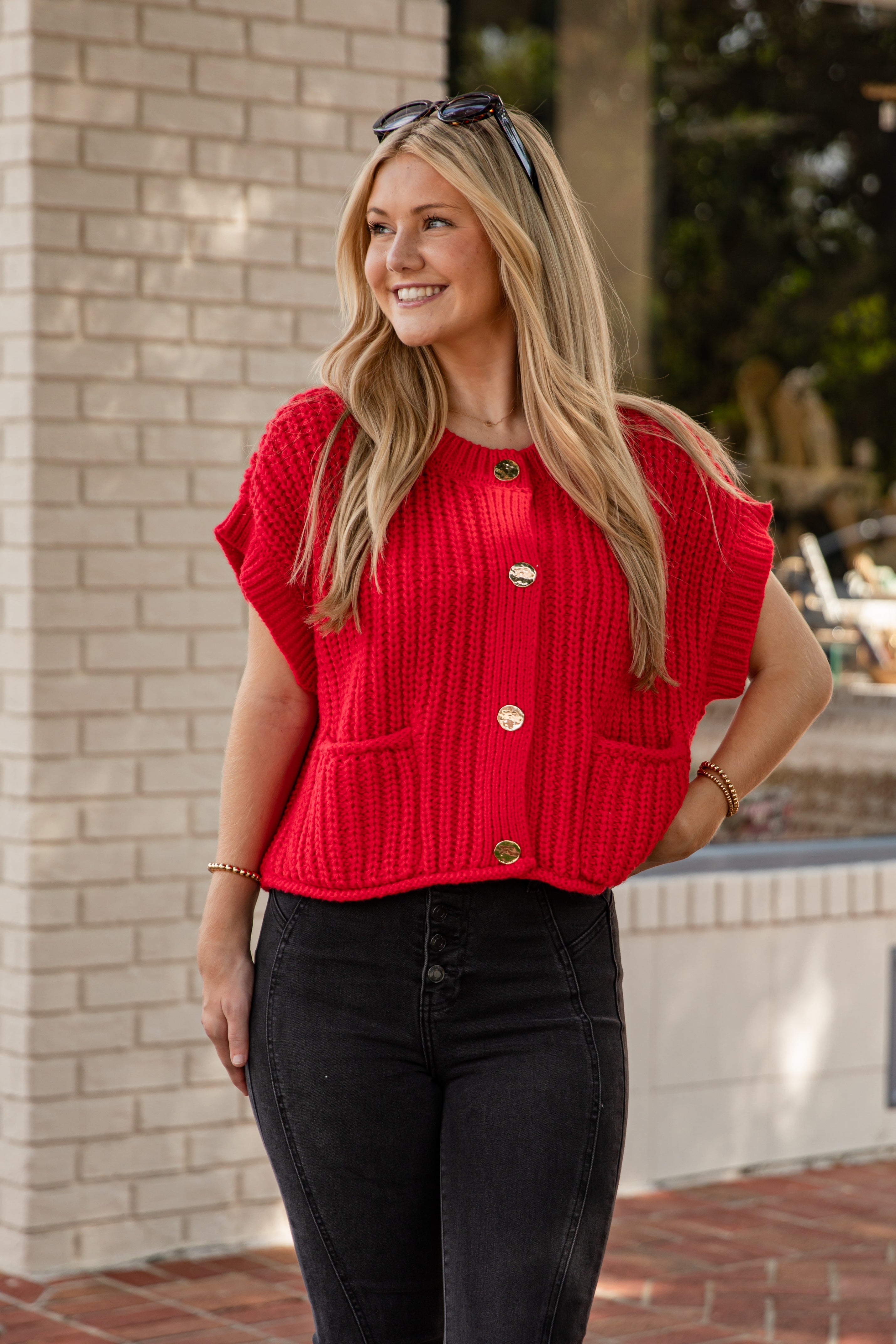 Woman wearing a red vest standing against a brick wall.