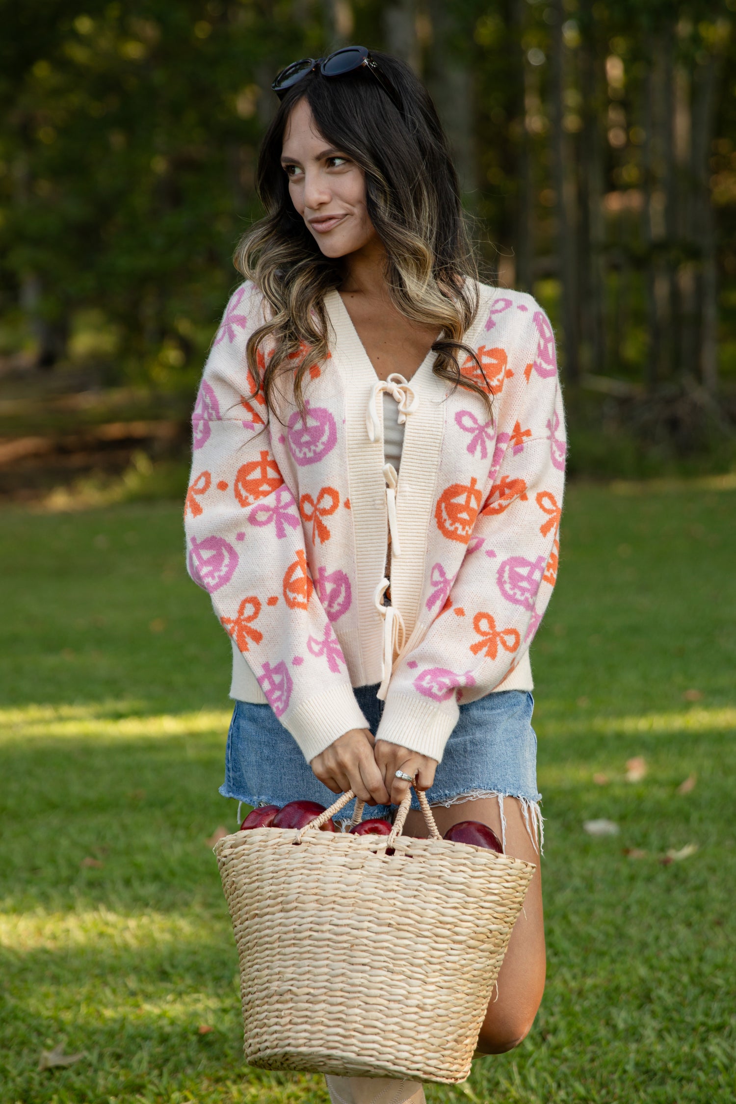 Woman holding a woven basket outdoors with a colorful patterned cardigan.