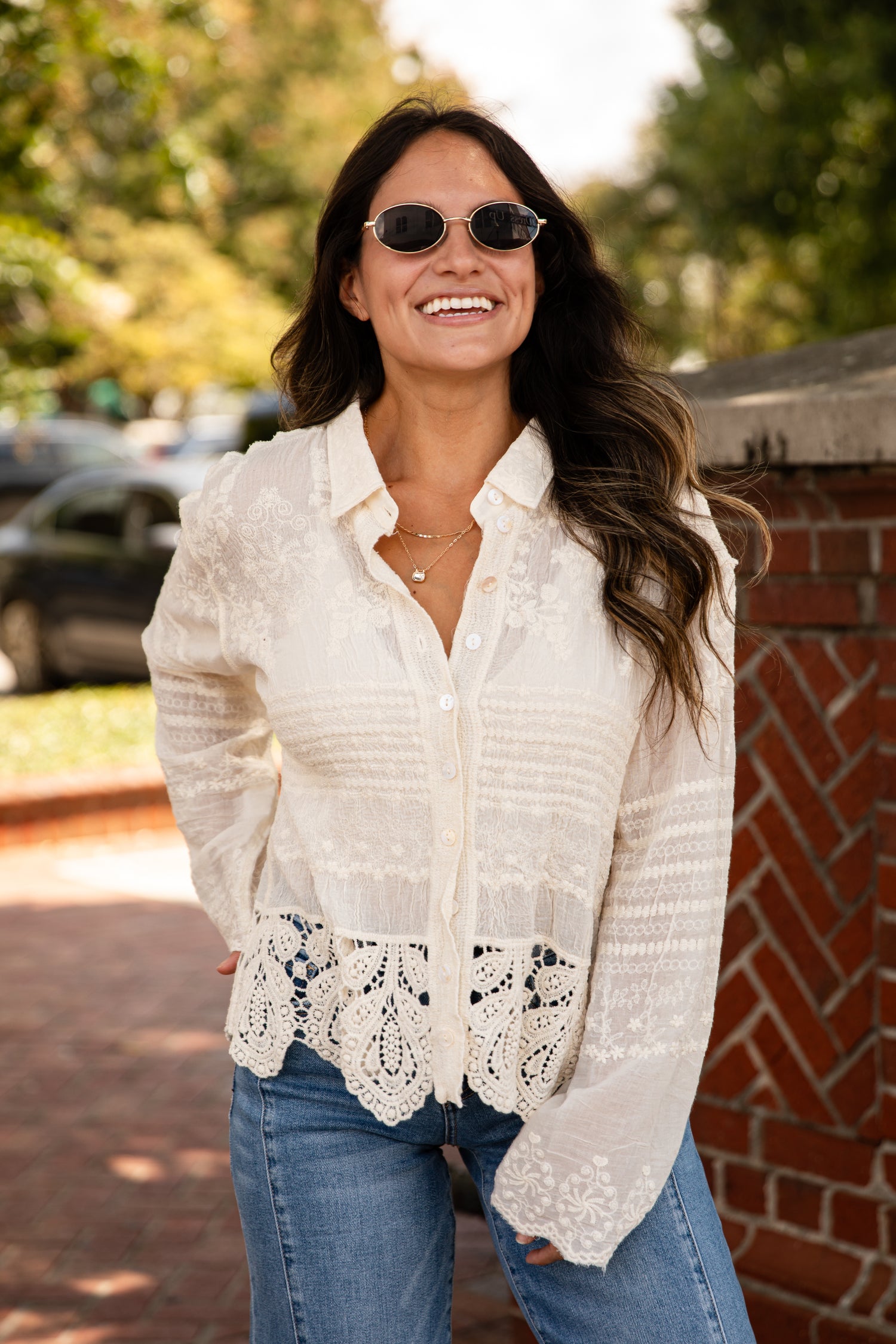 Woman wearing a white lace blouse and sunglasses outdoors.