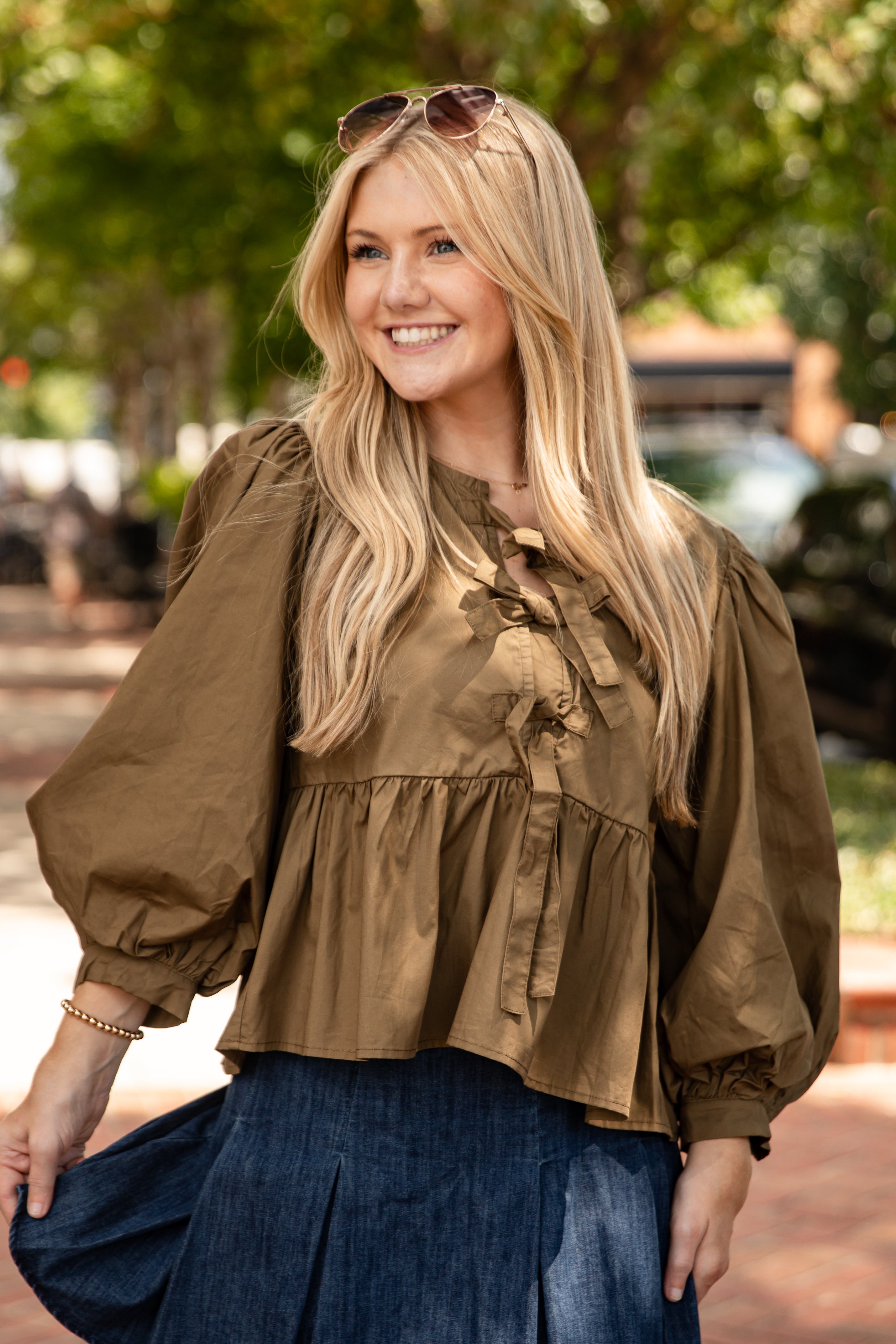 Woman wearing a brown blouse and blue skirt outdoors with trees in the background