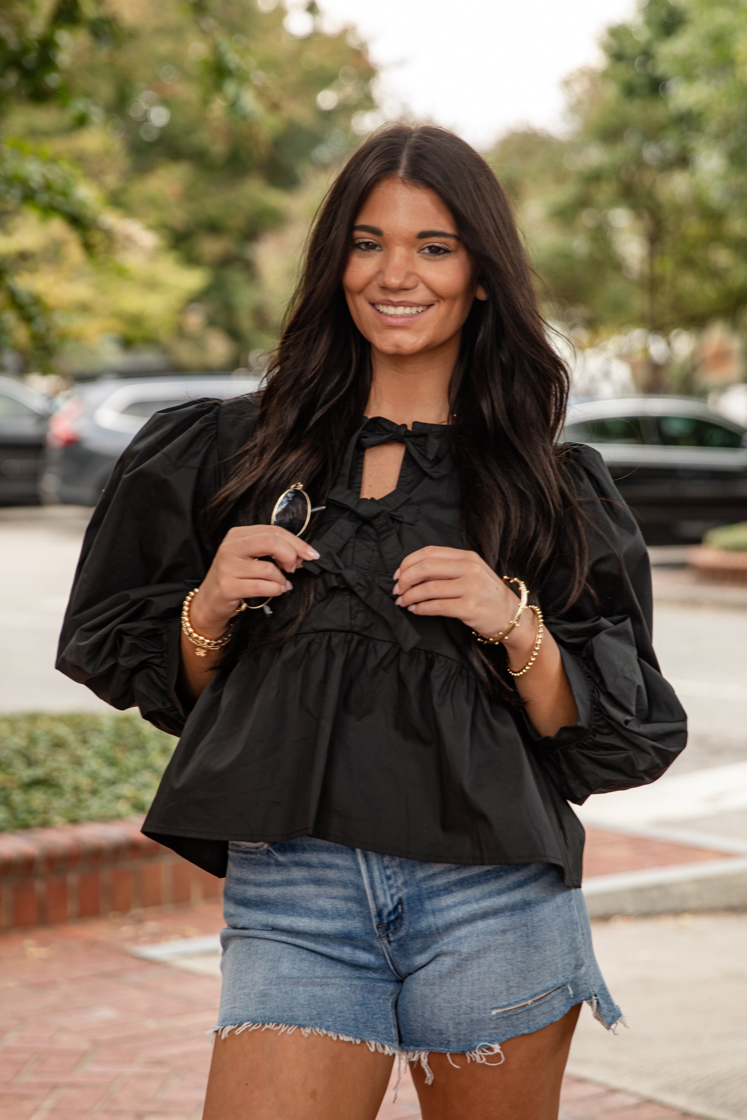 Woman wearing a black blouse with ruffled details and denim shorts outdoors.