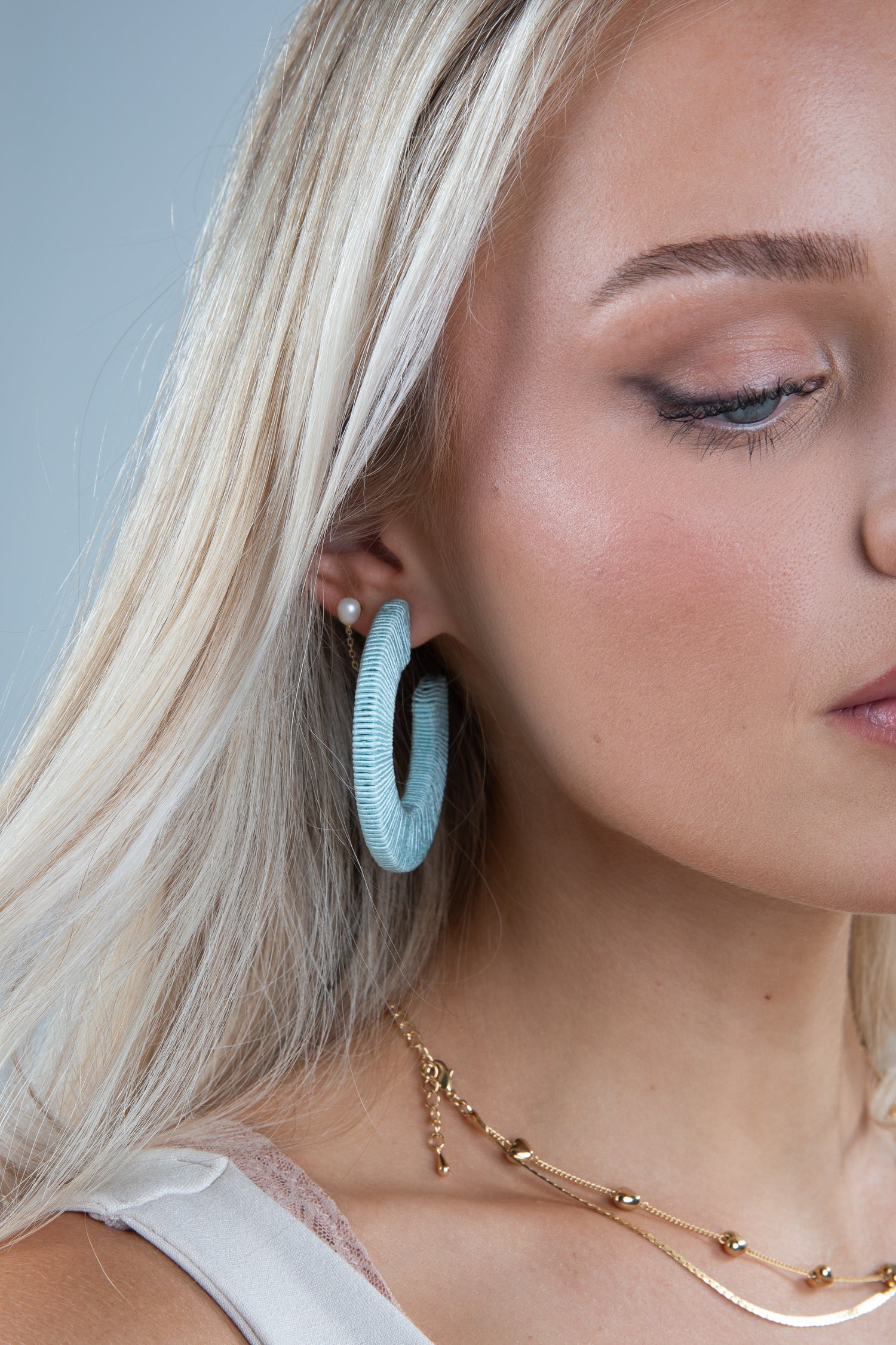 Close-up of a woman wearing light blue hoop earrings with a neutral background