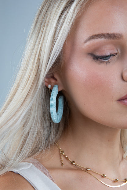 Close-up of a woman wearing light blue hoop earrings with a neutral background