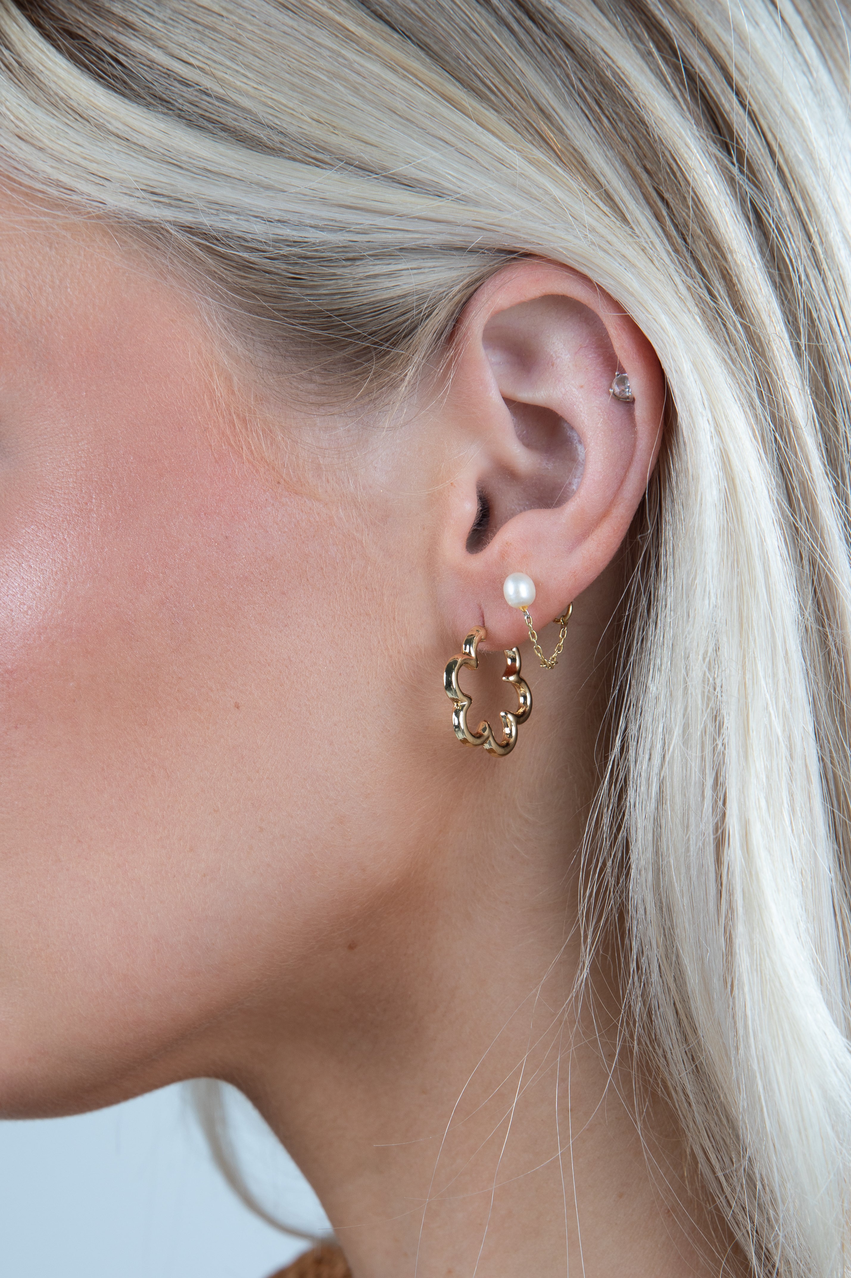 Close-up of a person wearing gold hoop earrings with a pearl accent.