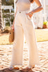 Person wearing cream-colored pants and a beige top, standing on a paved walkway.