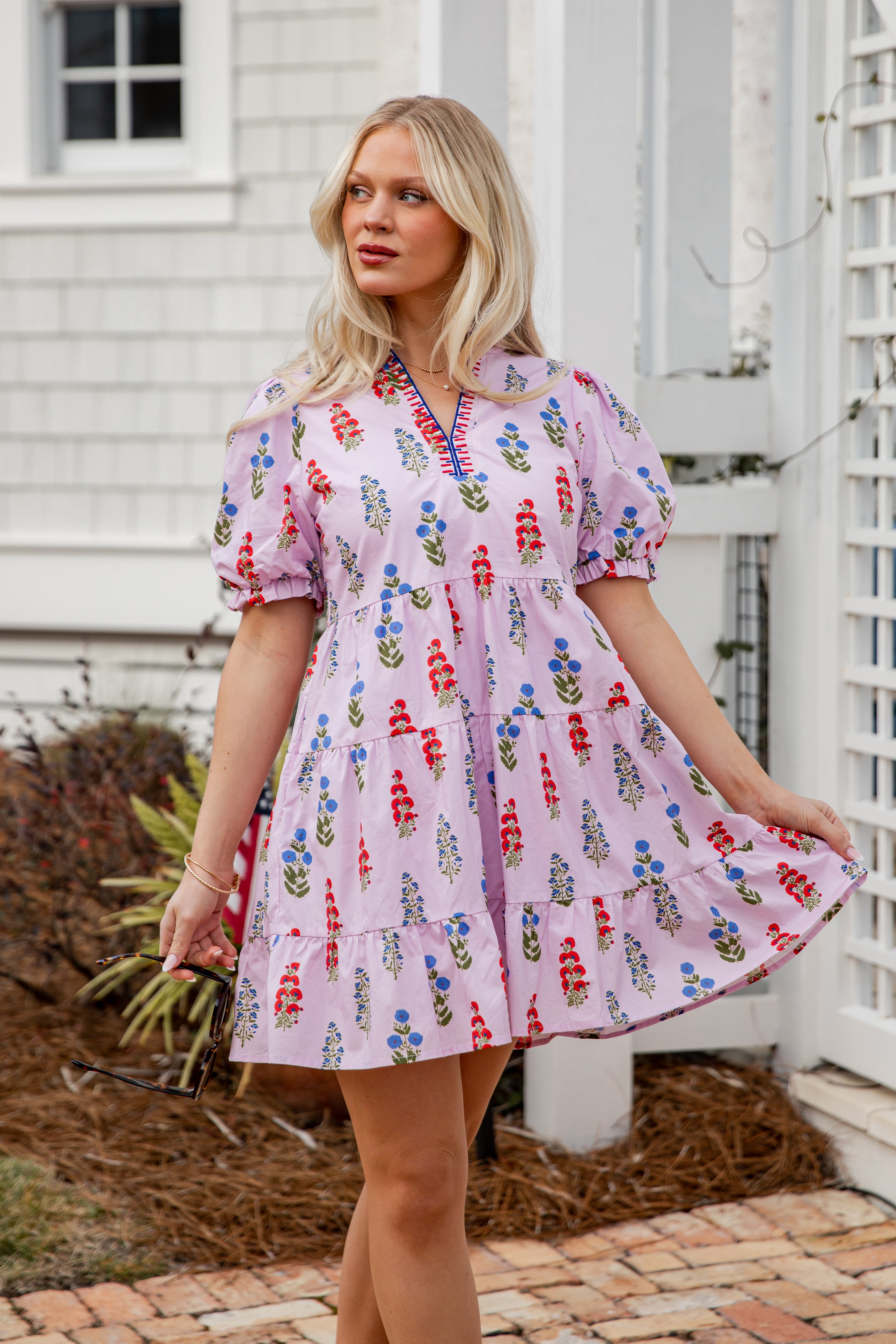 Woman wearing a pink floral dress standing outdoors near a white building.