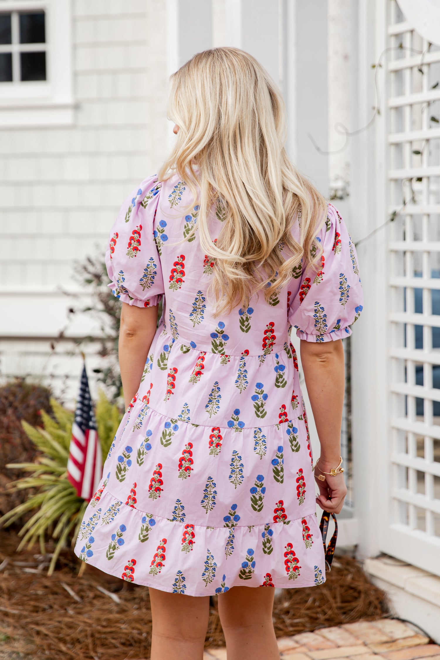 Woman wearing a floral dress standing in front of a white building with an American flag.