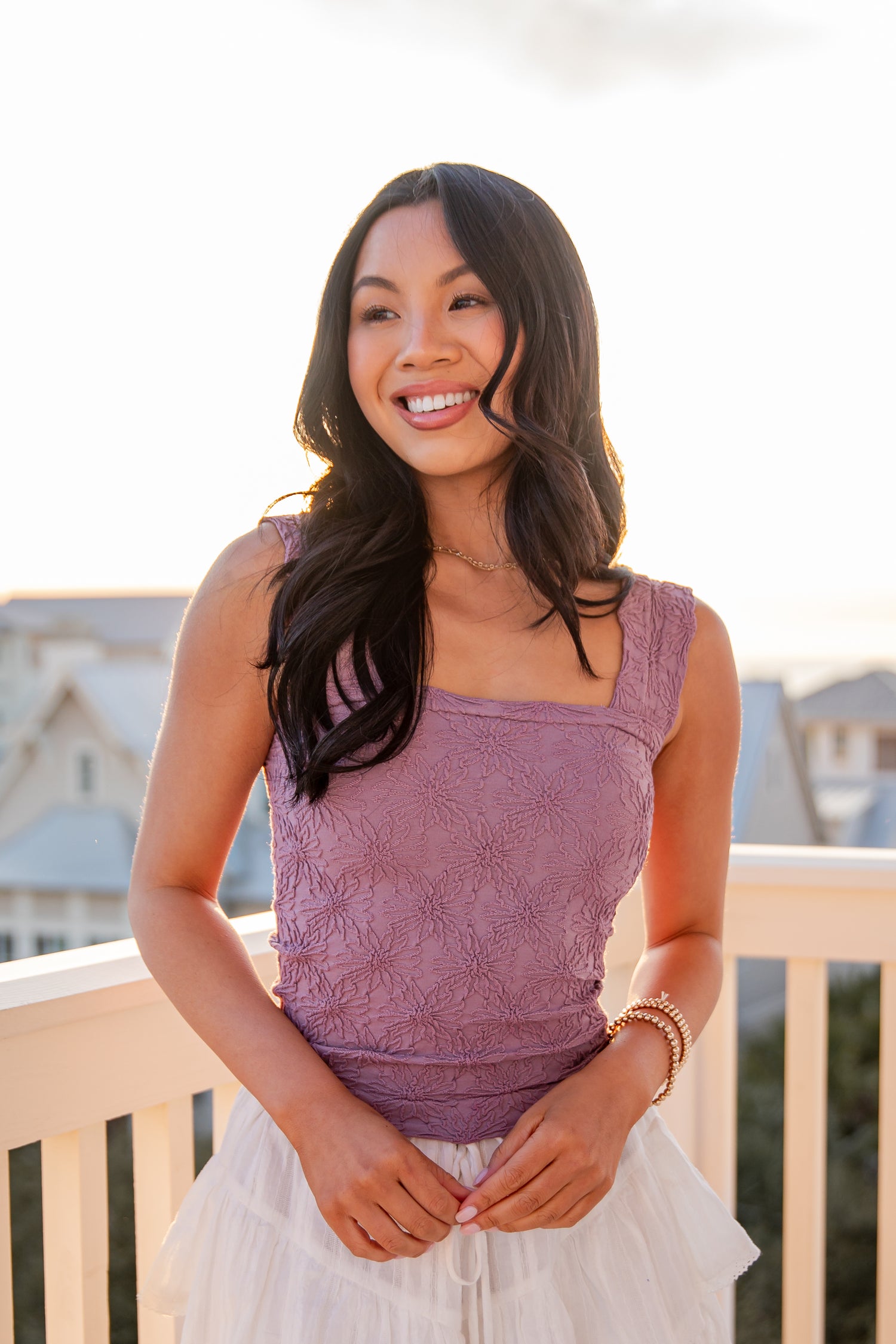 Woman wearing a purple top and white skirt on a balcony with a blurred background