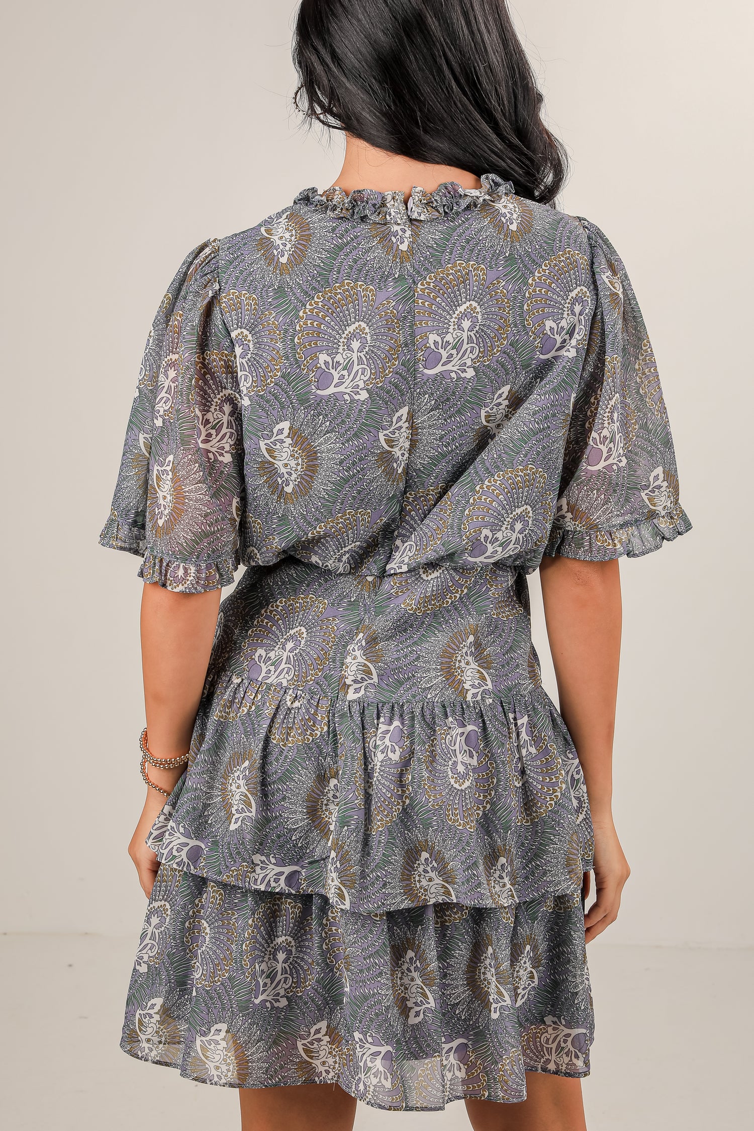 Woman wearing a patterned dress with ruffled layers on a plain background