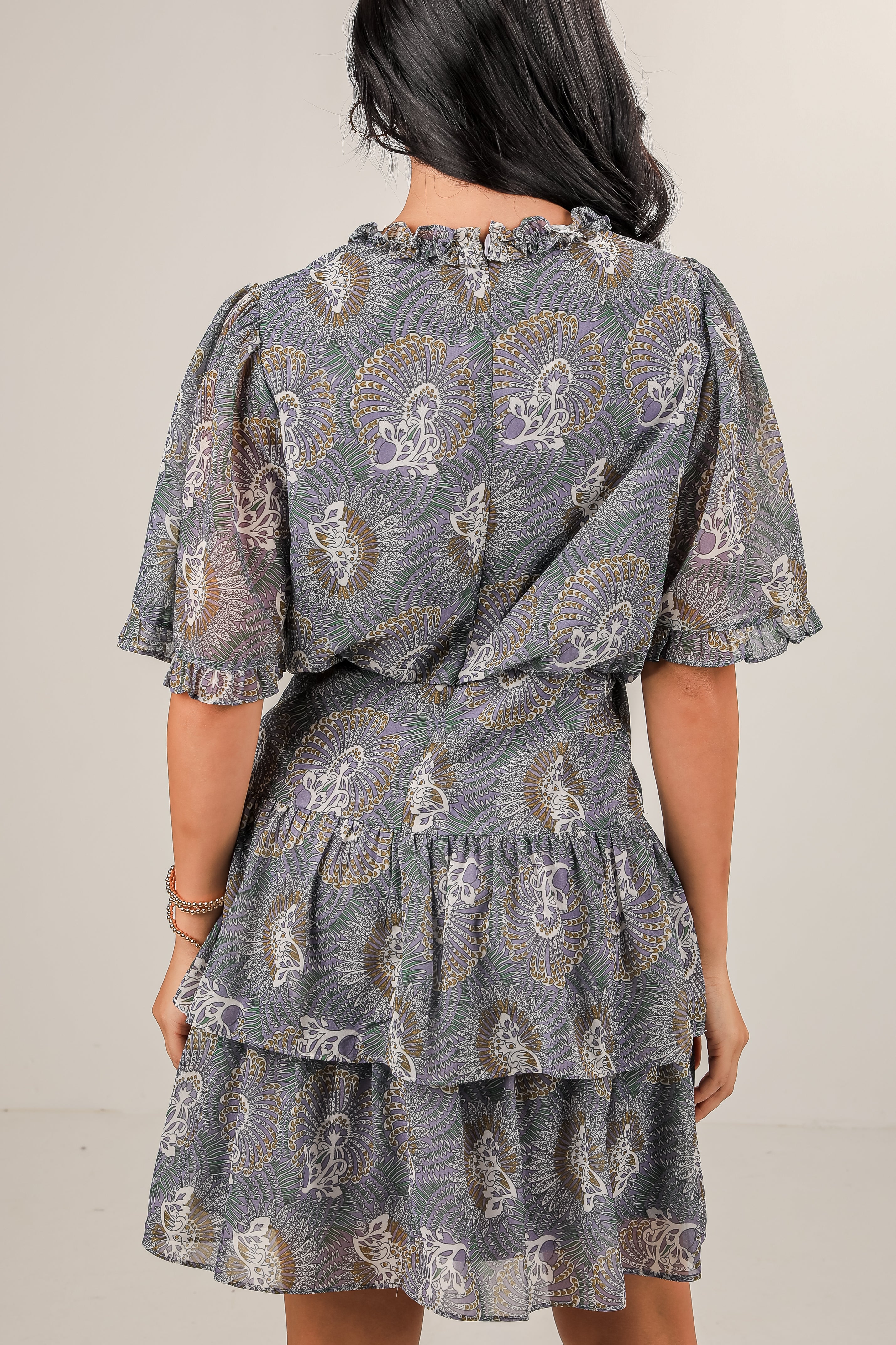 Woman wearing a patterned dress with ruffled layers on a plain background