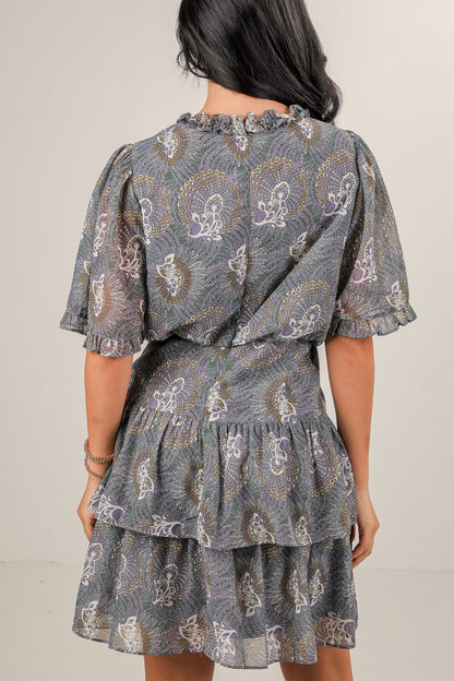 Woman wearing a patterned dress with ruffled layers on a plain background