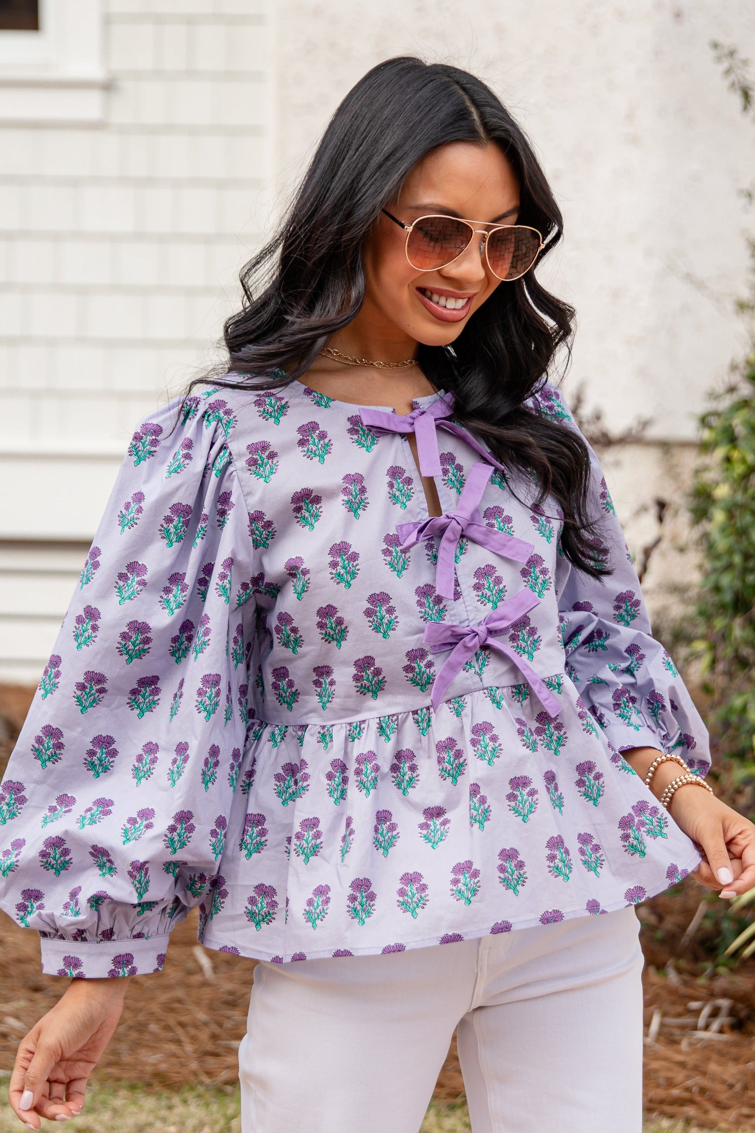 Woman wearing a floral blouse with a bow tie in front of a white building.