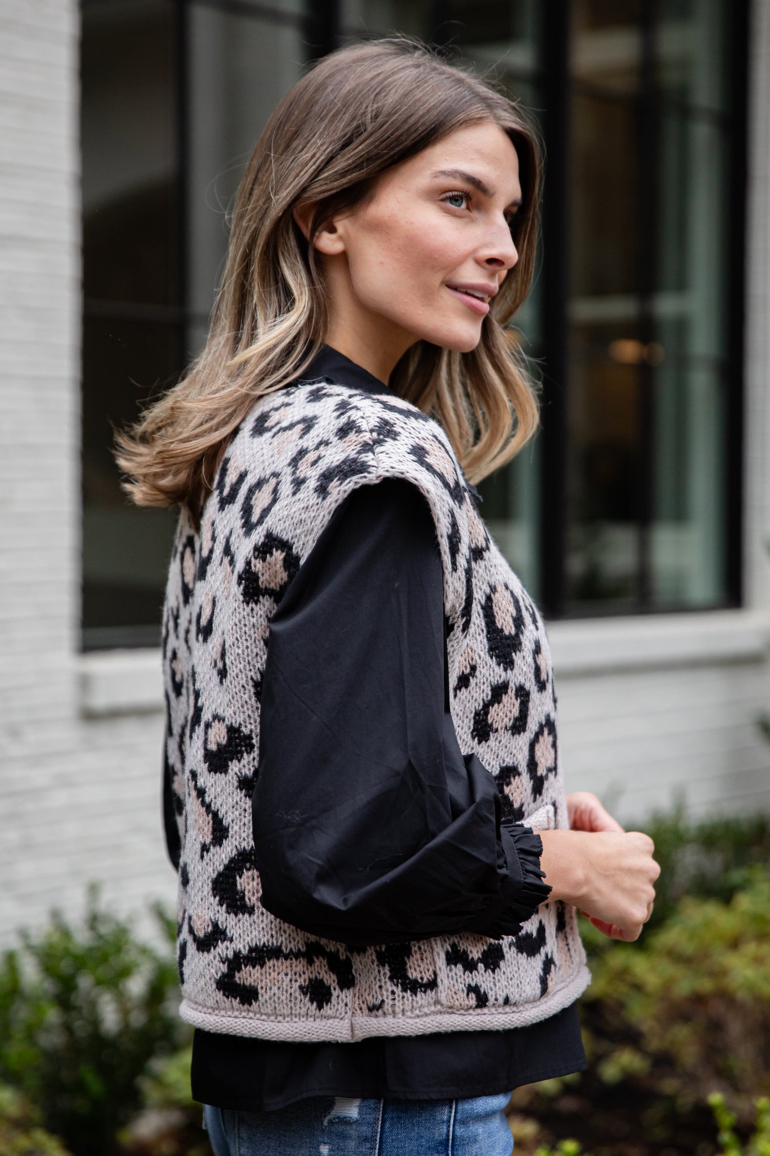 Woman wearing a leopard print vest over a black top outdoors.