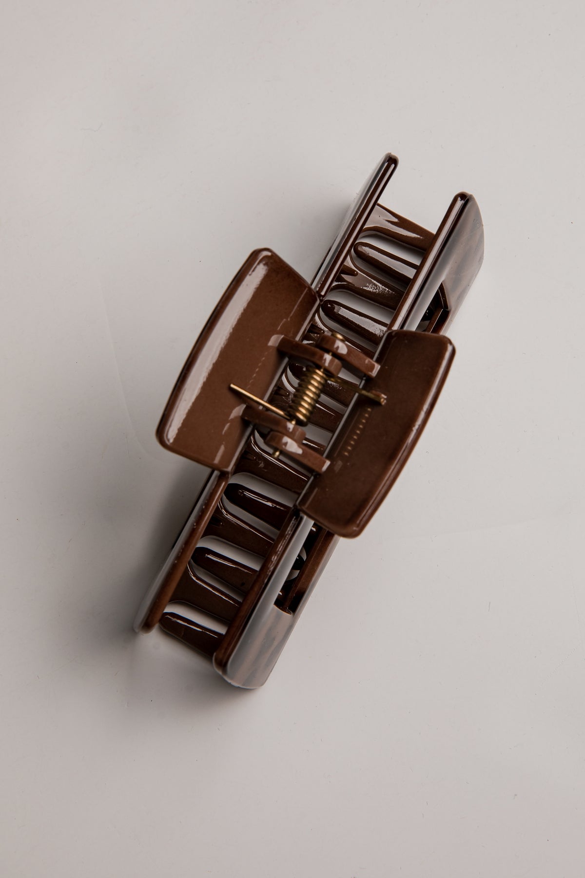 A glossy dark brown hair claw clip shown from an overhead angle on a light gray background.