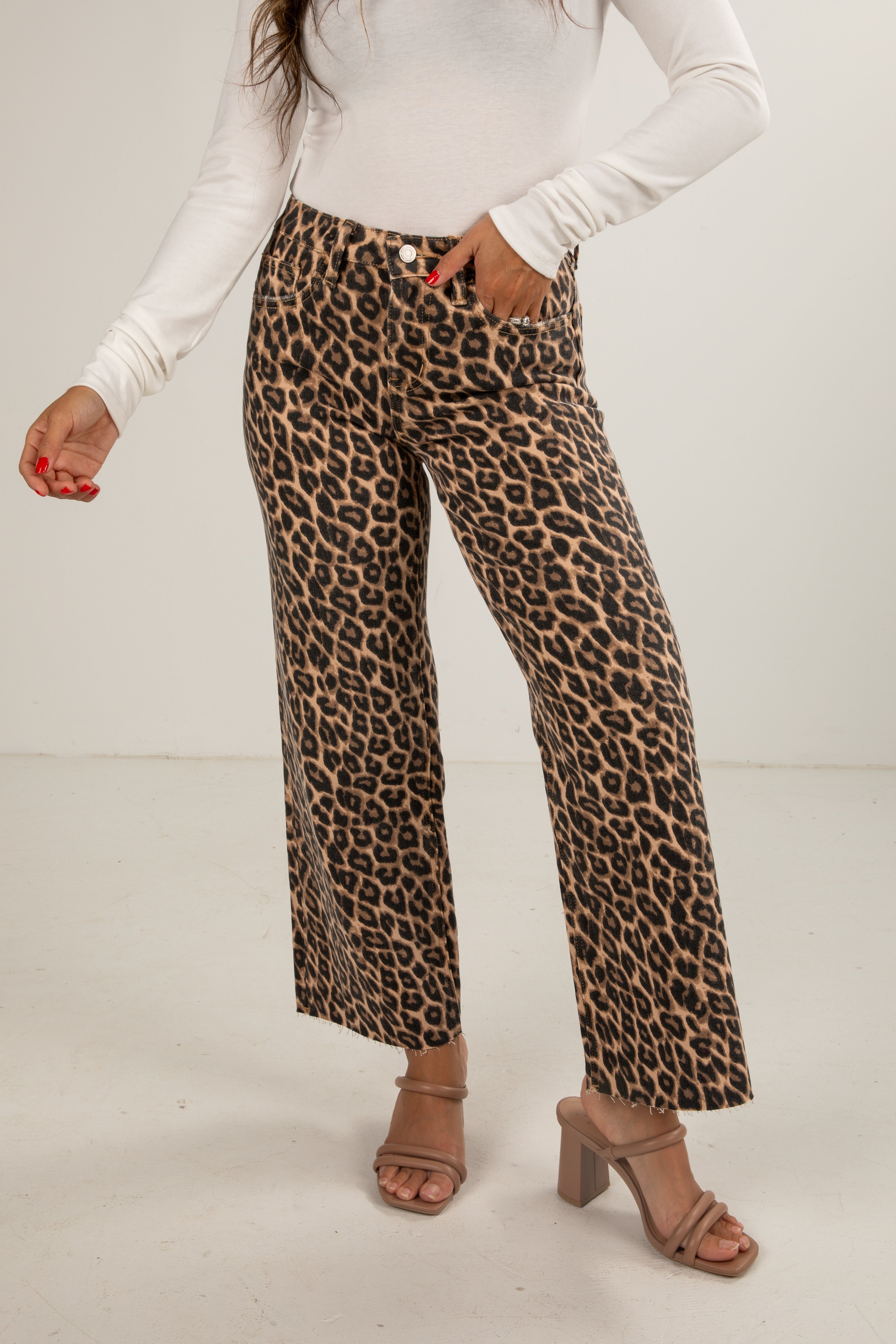Person wearing leopard print pants with a white top on a plain background