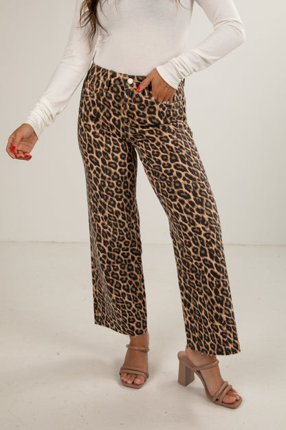 Person wearing leopard print pants with a white top on a plain background