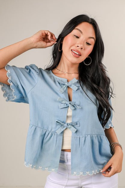 Woman wearing a light blue denim top with ruffled sleeves and hem on a plain background