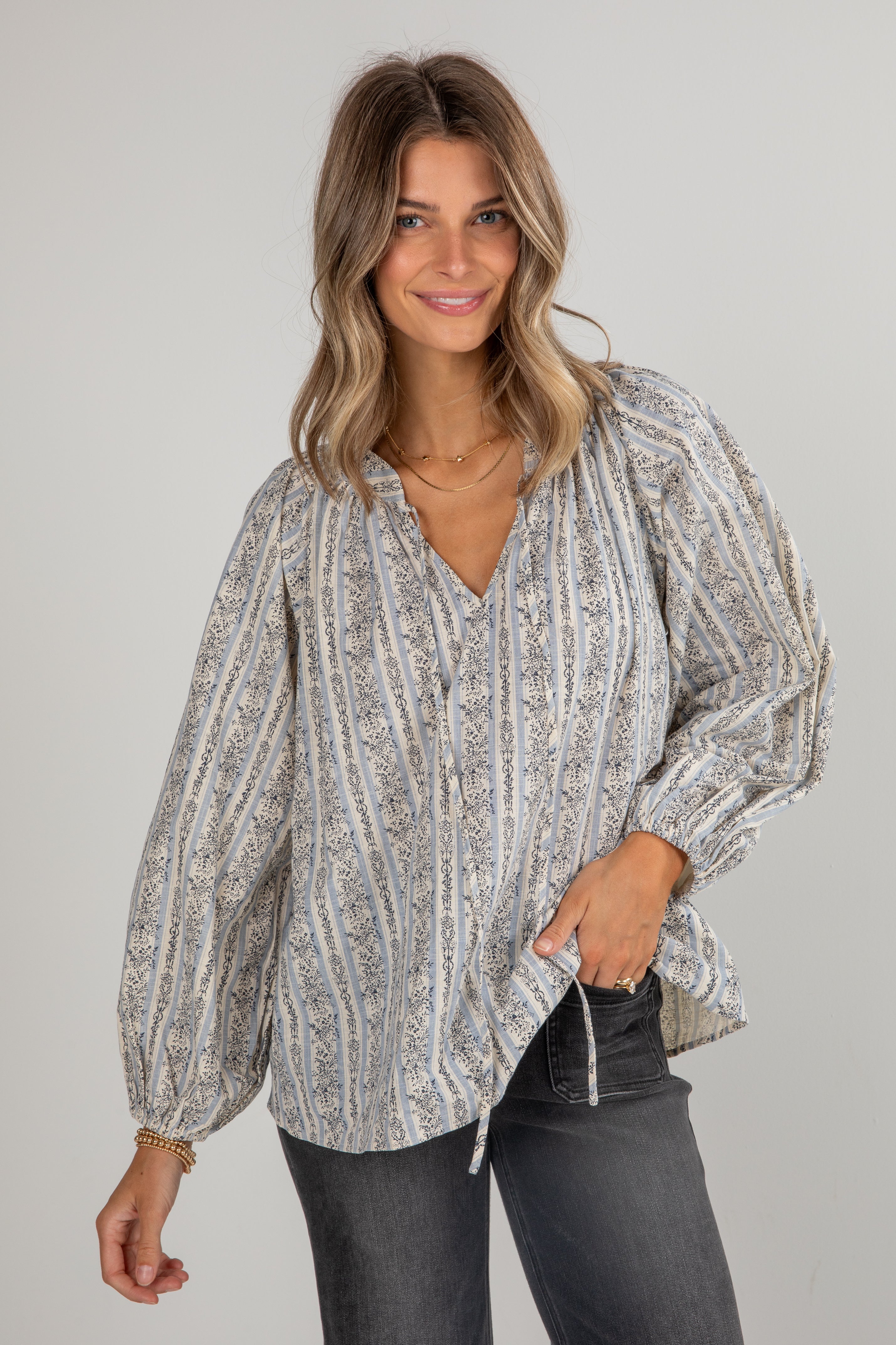 Woman wearing a patterned blouse and dark jeans on a plain background