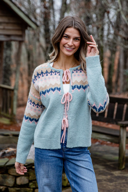Woman wearing a patterned cardigan outdoors with a wooden cabin in the background