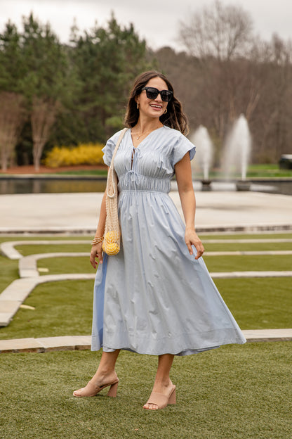 Woman in a light blue dress standing in a park with a fountain in the background