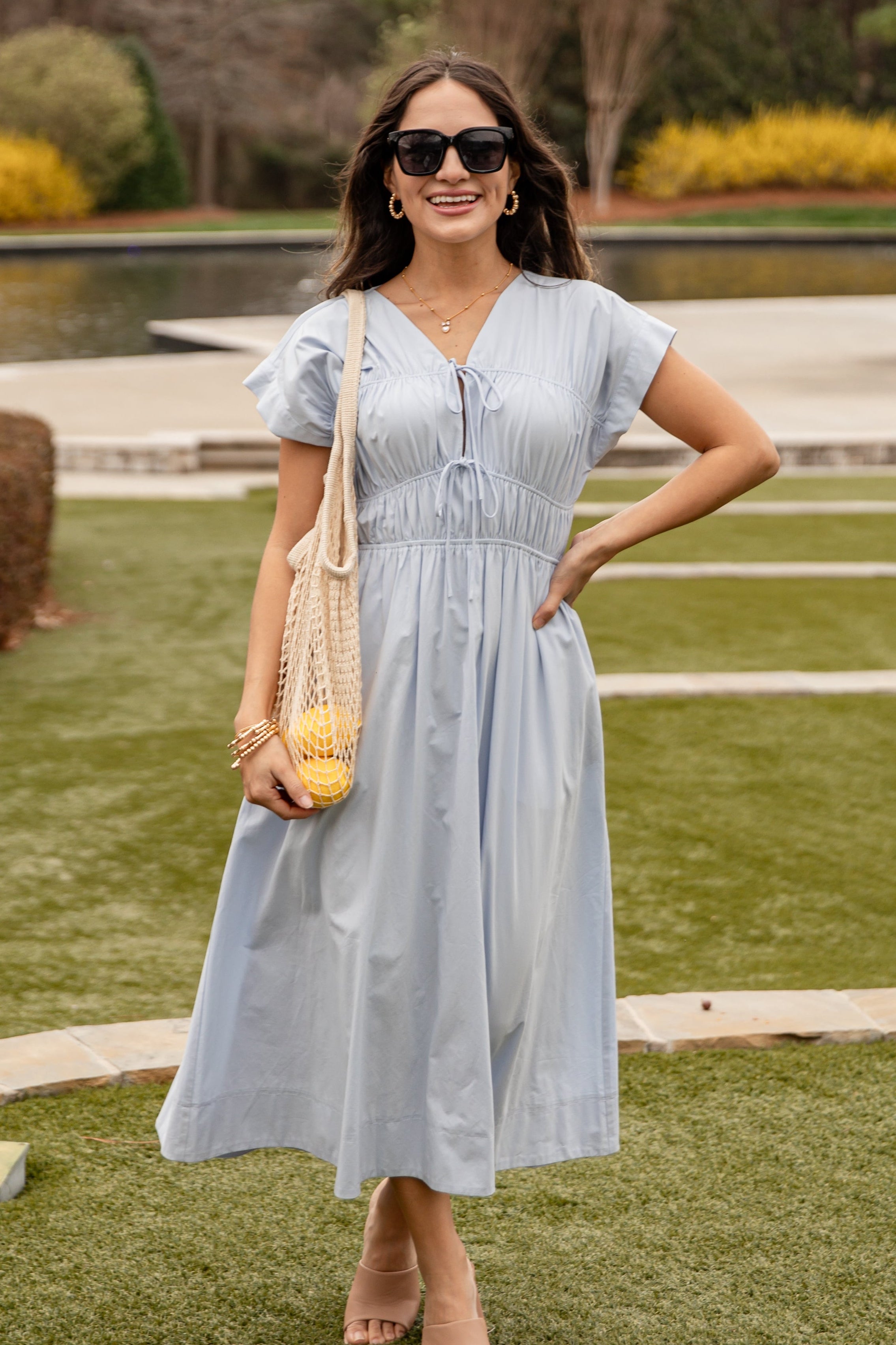 Woman in a light blue dress standing outdoors with a yellow bag.