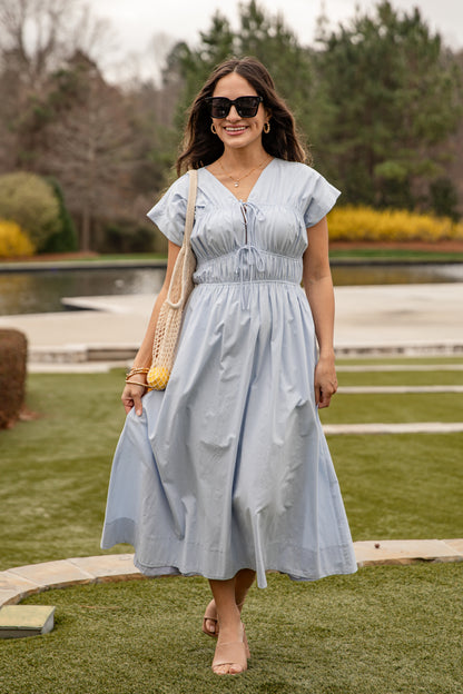 Woman in a light blue dress walking outdoors with a scenic background