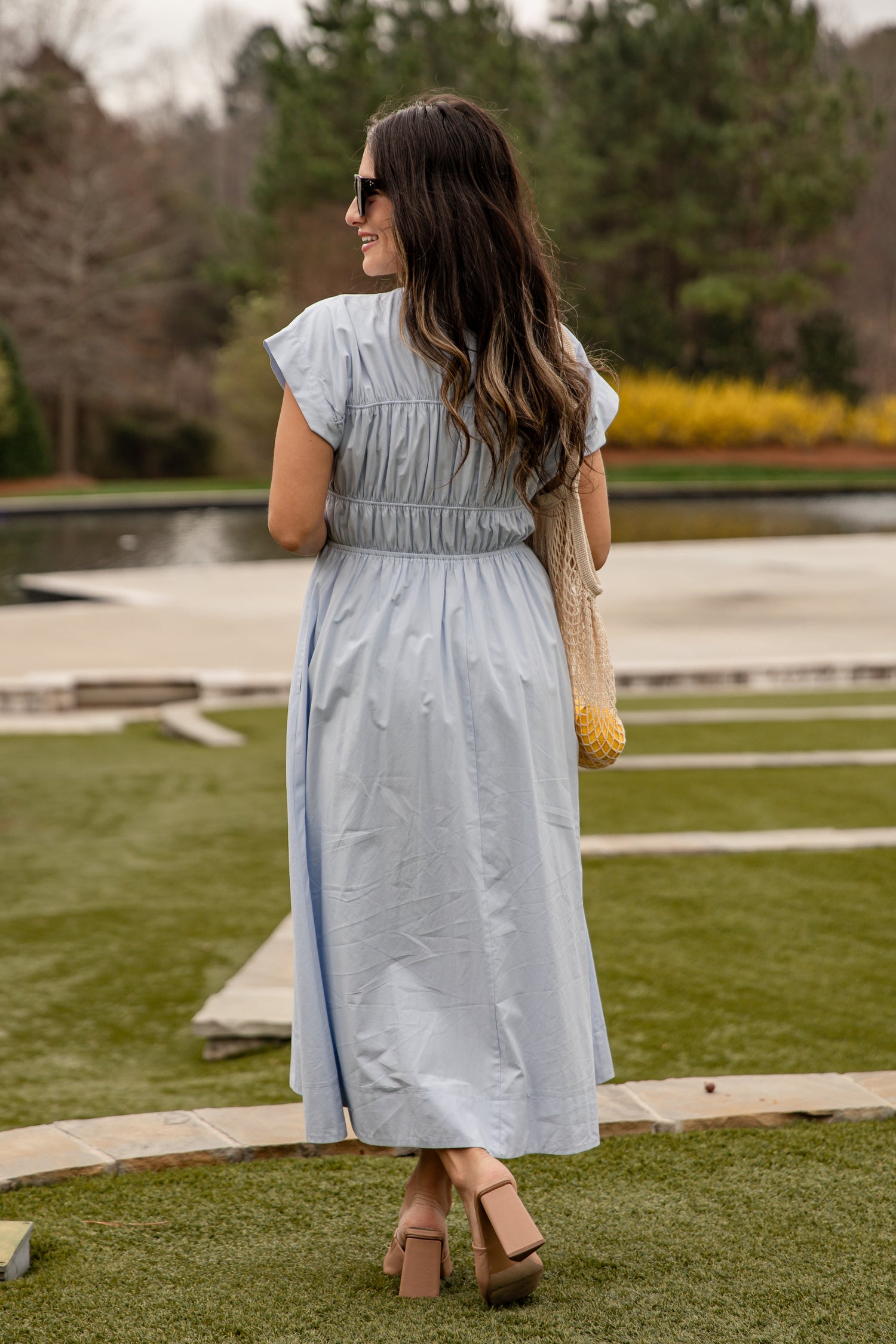 Woman in a light blue dress standing on grass with trees in the background