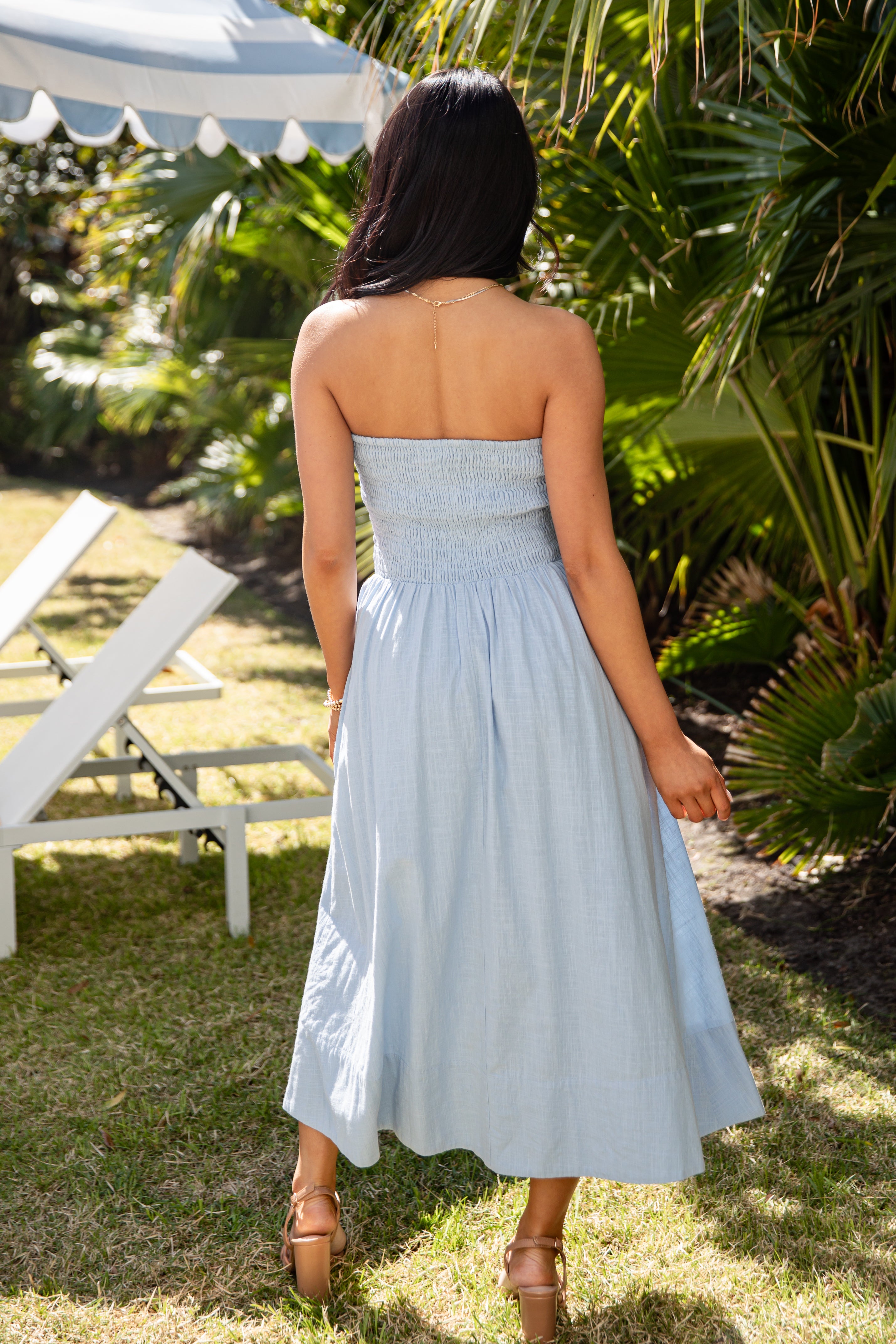 Woman in a light blue dress standing outdoors with greenery and a white tent in the background