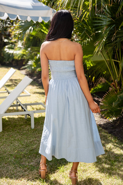 Woman in a light blue dress standing outdoors with greenery and a white tent in the background