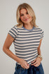 A woman wearing a fitted short-sleeve striped t-shirt with horizontal navy, slate blue, and off-white stripes, paired with blue jeans, against a light gray brick wall background.