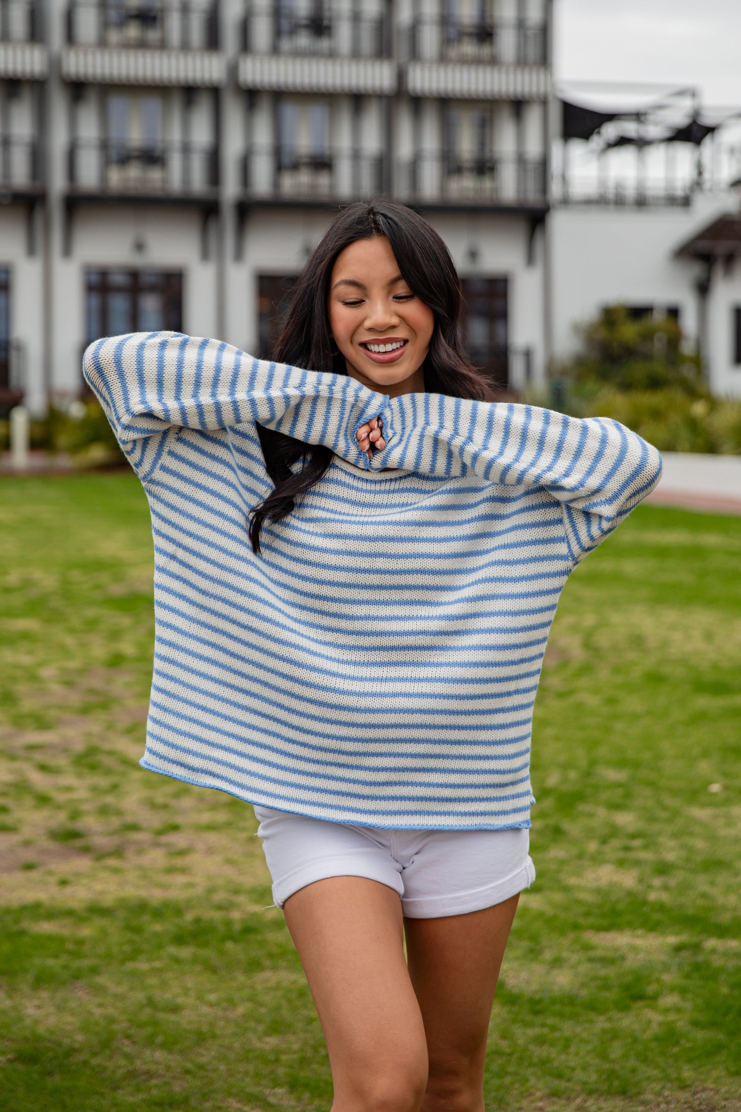 Woman wearing a blue and white striped sweater and white shorts outdoors.