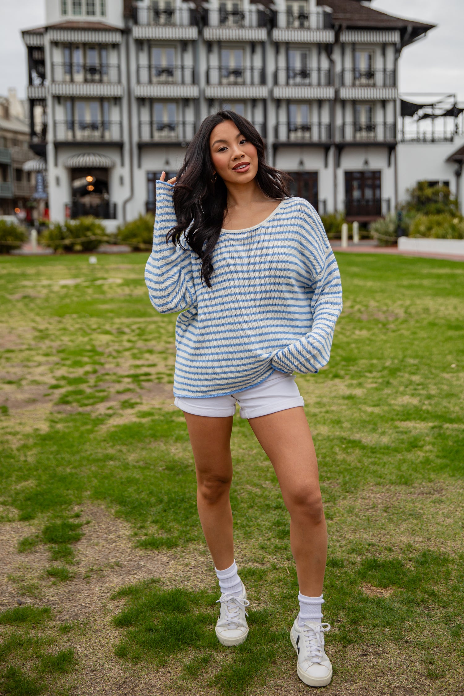 Woman in a striped sweater and shorts standing on grass with a building in the background