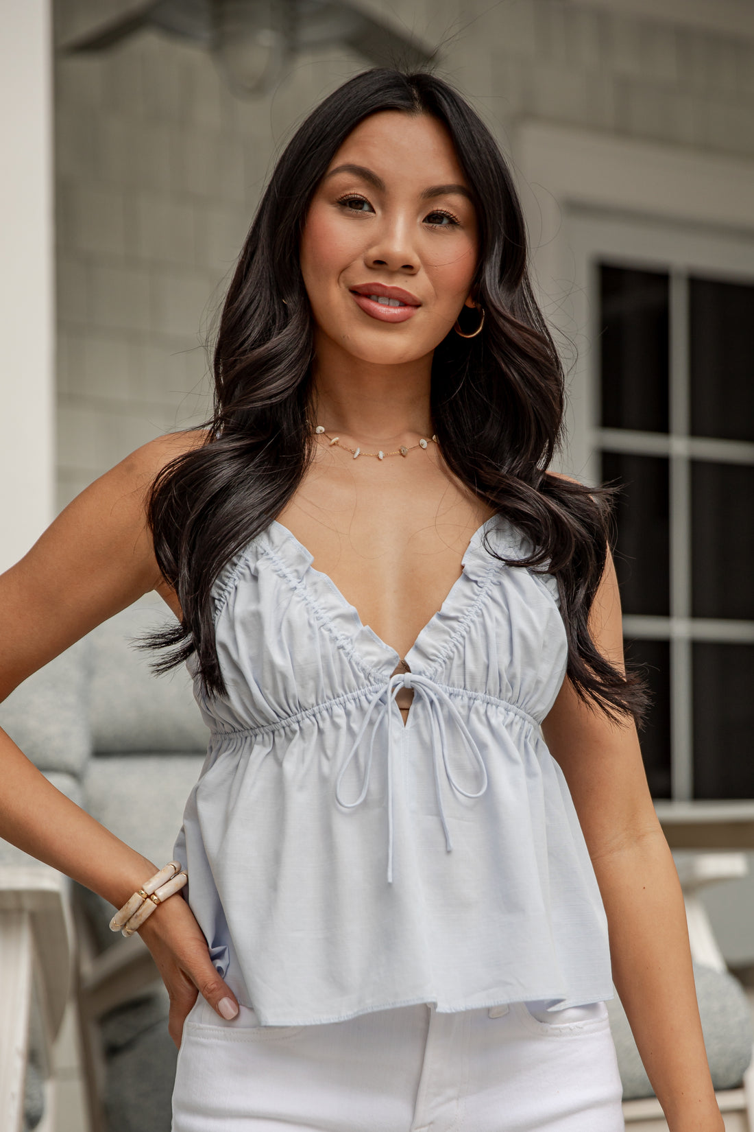 Woman wearing a light gray sleeveless top and white pants outdoors.