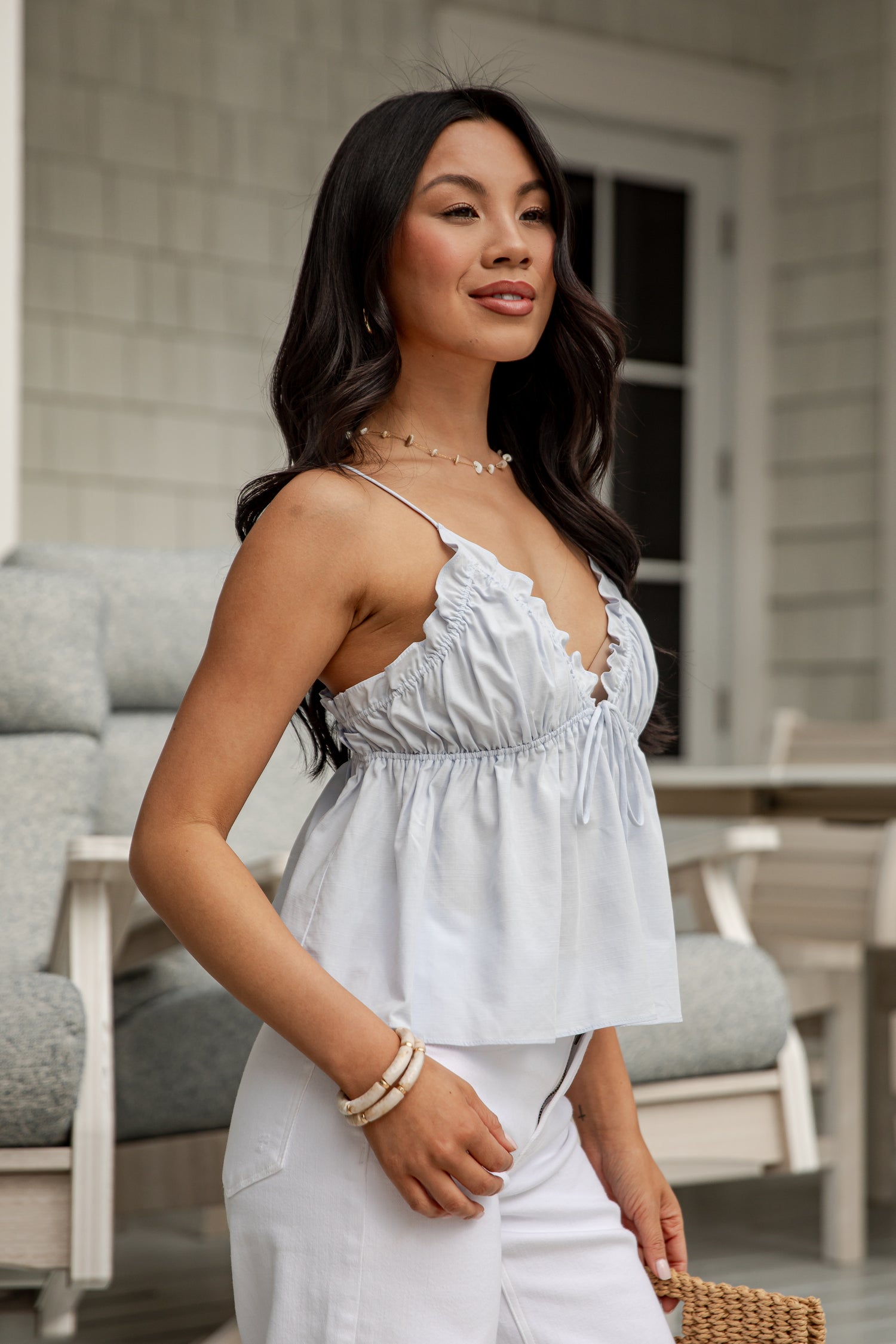 Woman wearing a light blue top and white pants on a patio