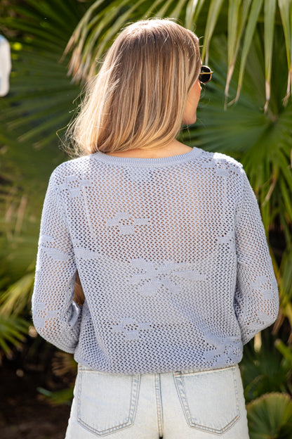 Woman wearing a light blue crochet top with a palm leaf background