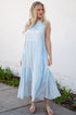 Woman wearing a light blue dress standing against a white wall.