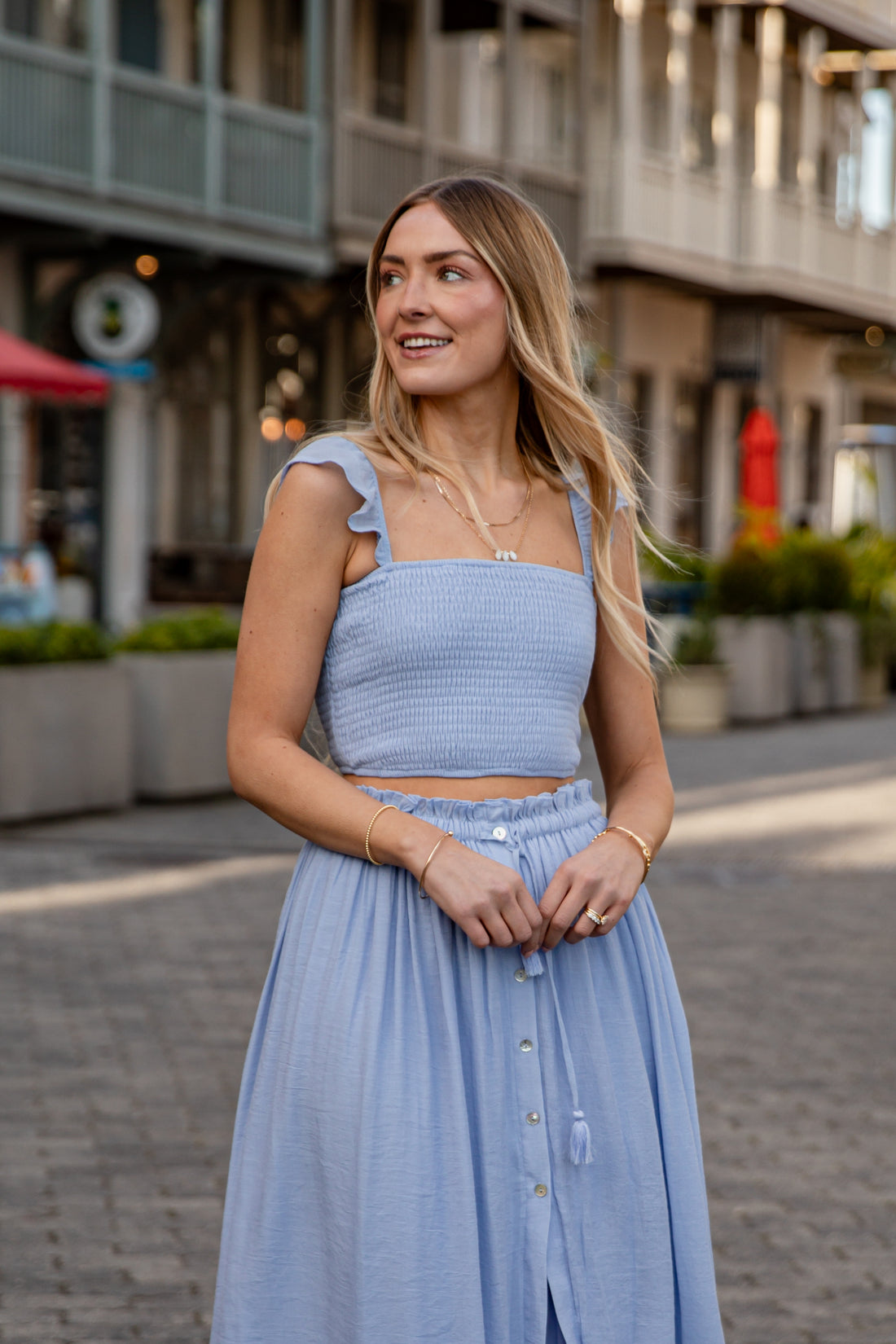 Woman in a light blue dress standing on a street with buildings in the background