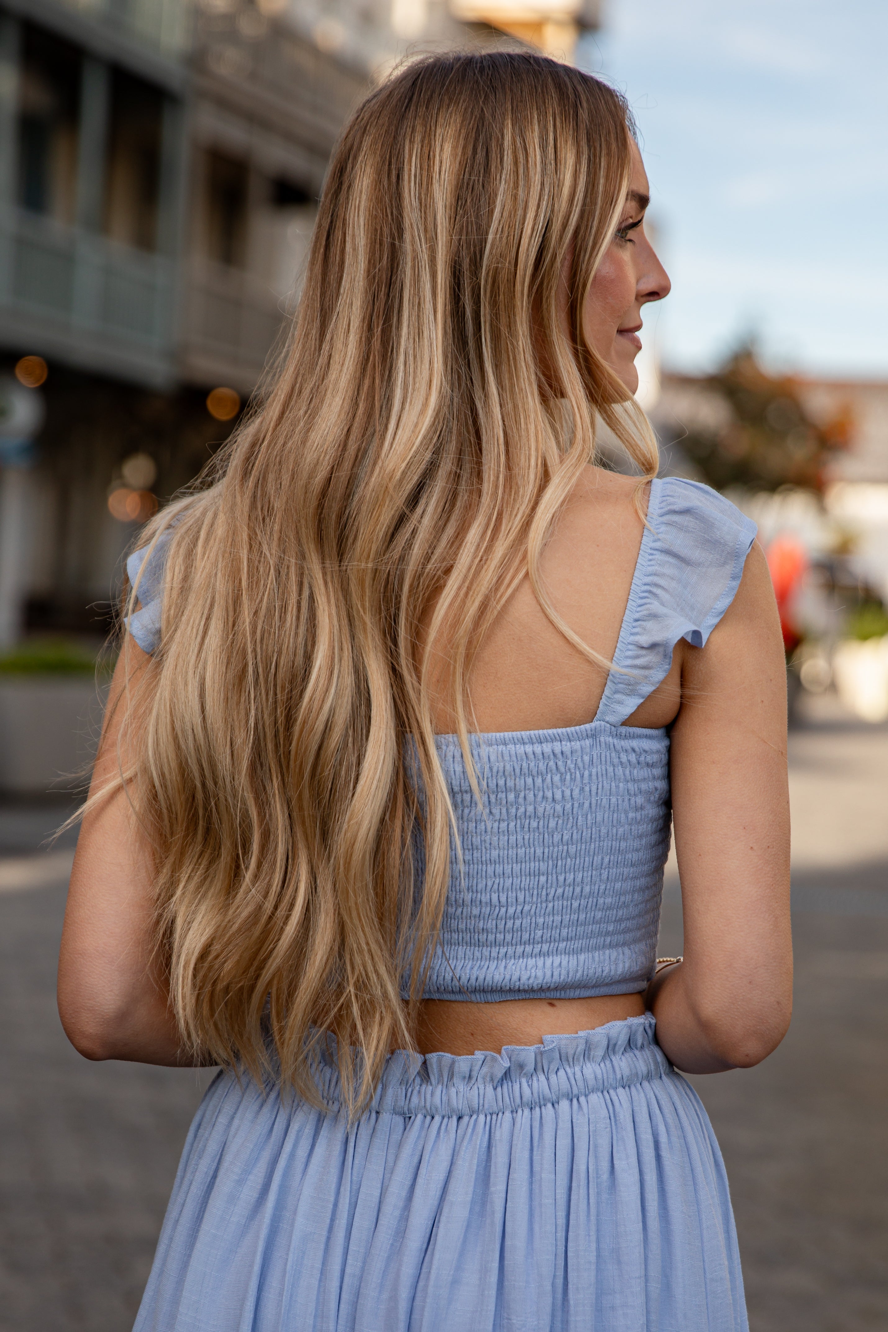 Woman in a light blue dress with ruffled sleeves standing on a street.