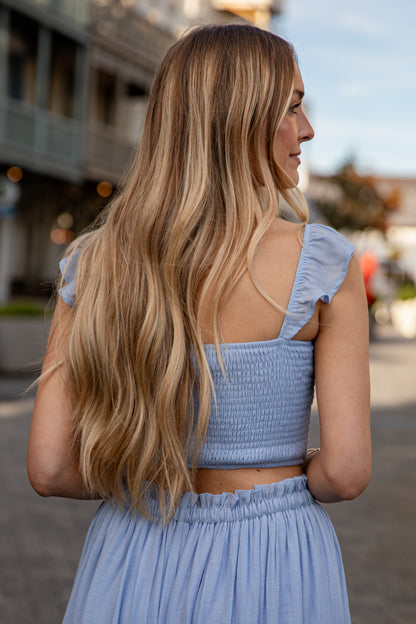 Woman in a light blue dress with ruffled sleeves standing on a street.