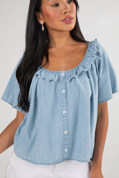 Woman wearing a light blue denim blouse with ruffled neckline on a white background