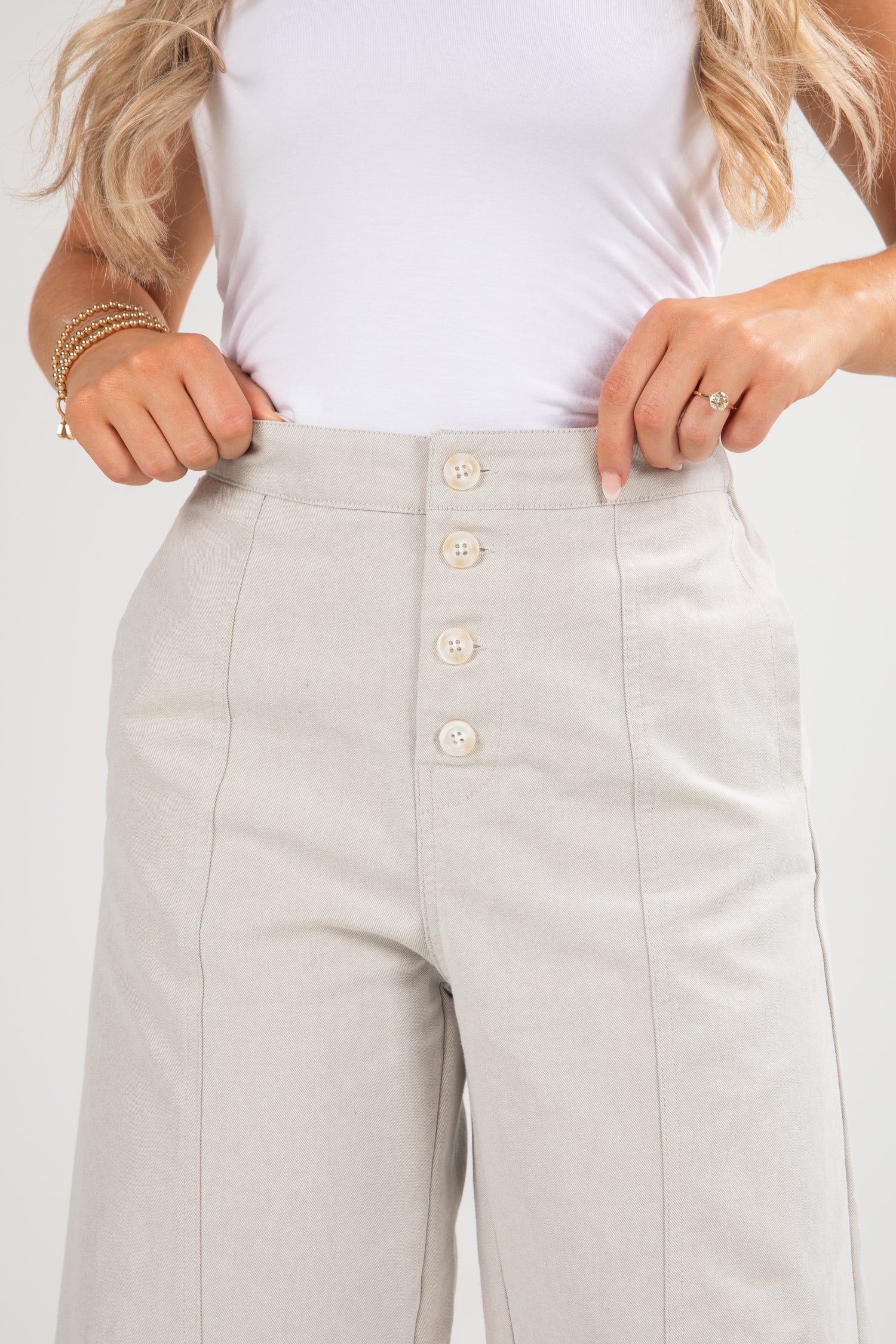 Light gray pants with button details worn by a person on a white background