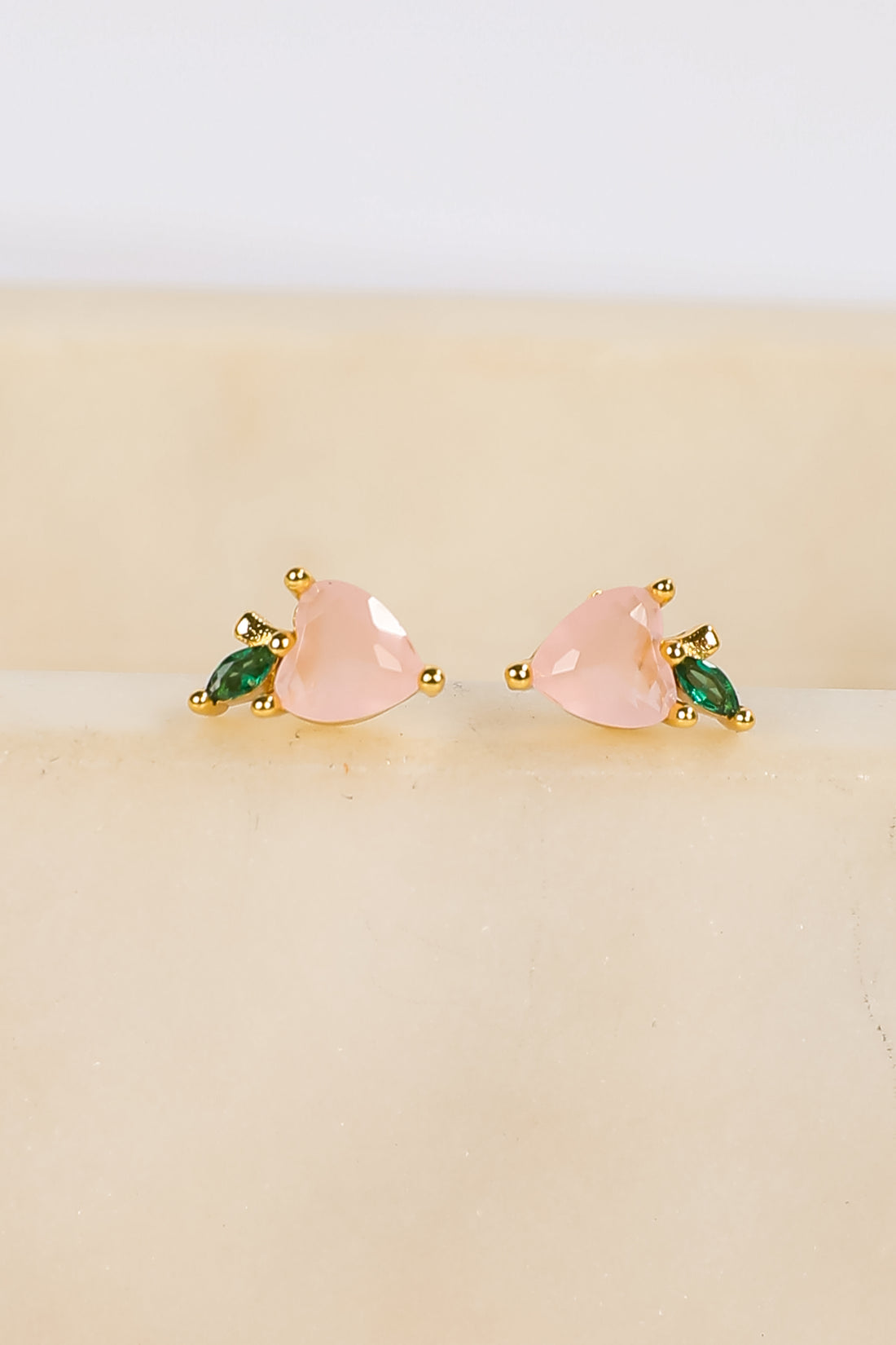 Pair of earrings with pink and green stones on a beige background