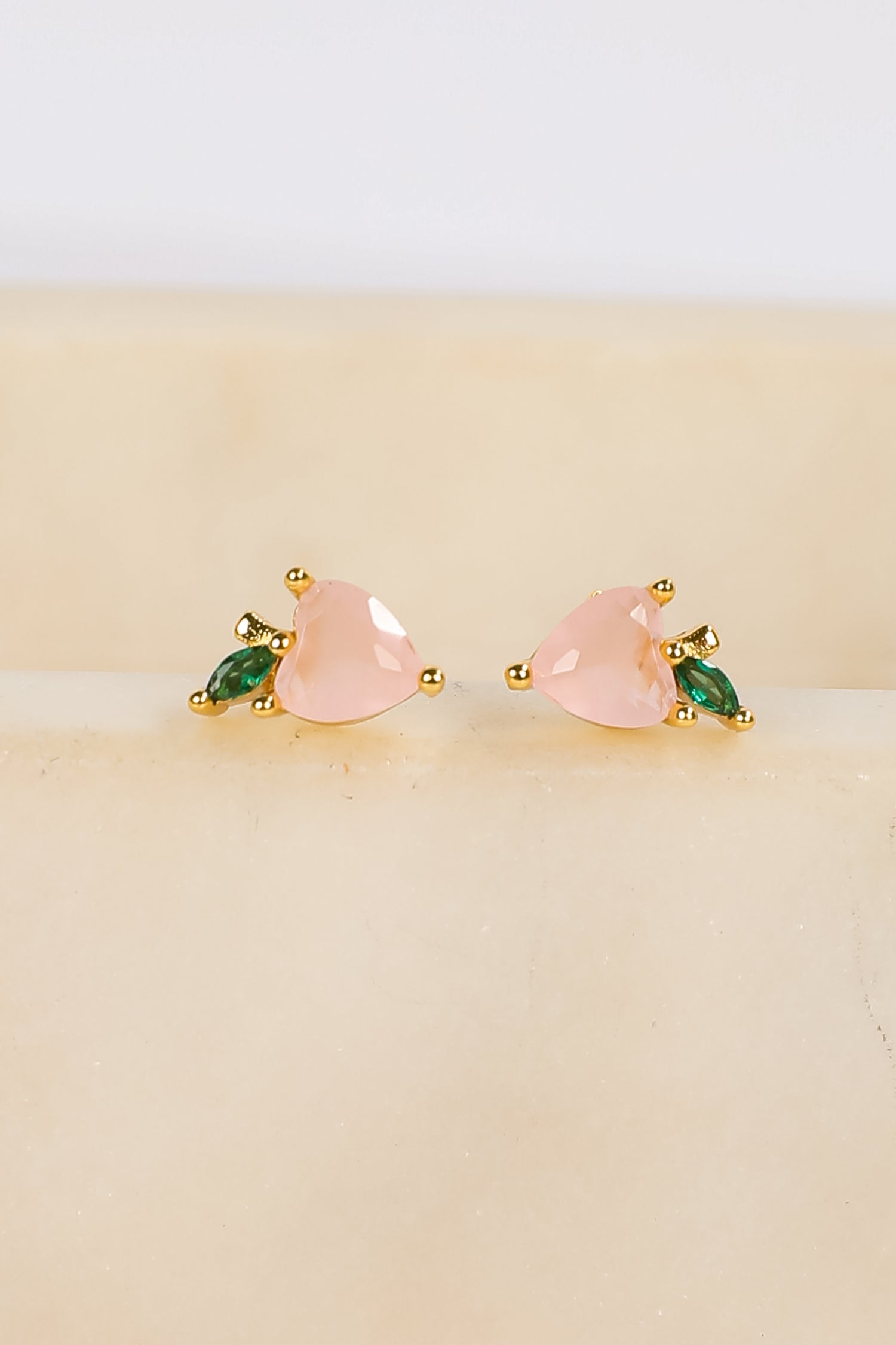 Pair of earrings with pink and green stones on a beige background