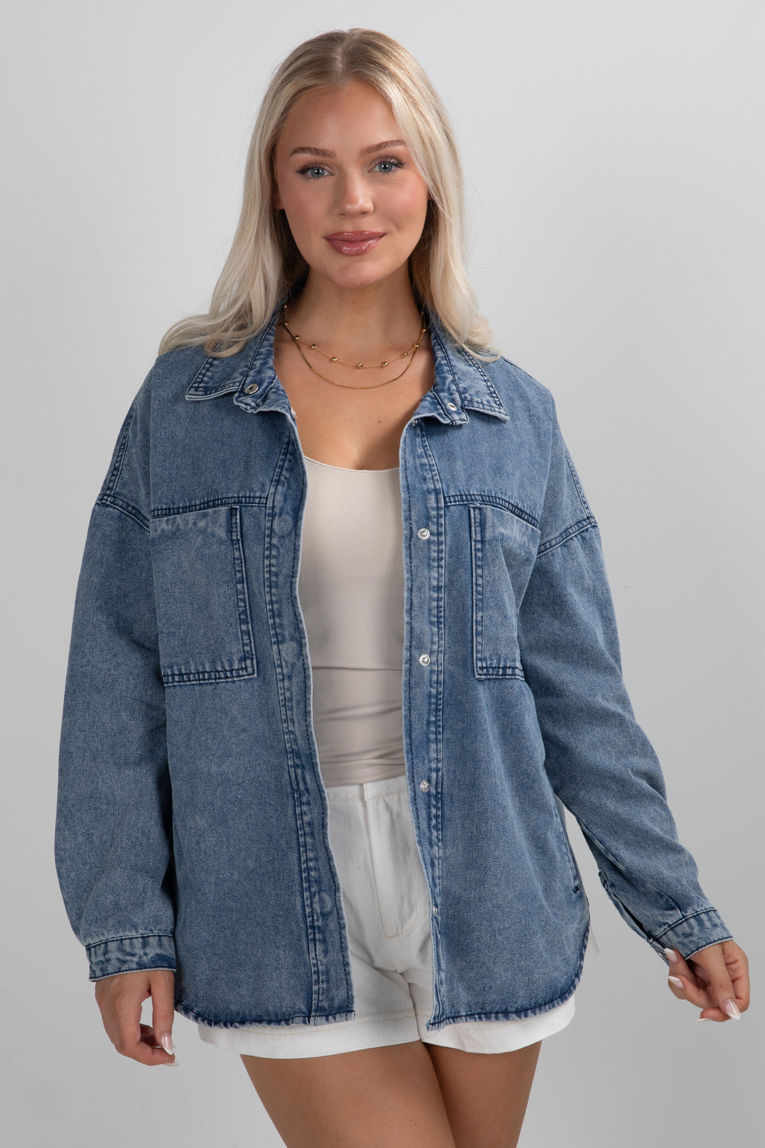 Woman wearing a blue denim jacket over a white top and shorts on a gray background