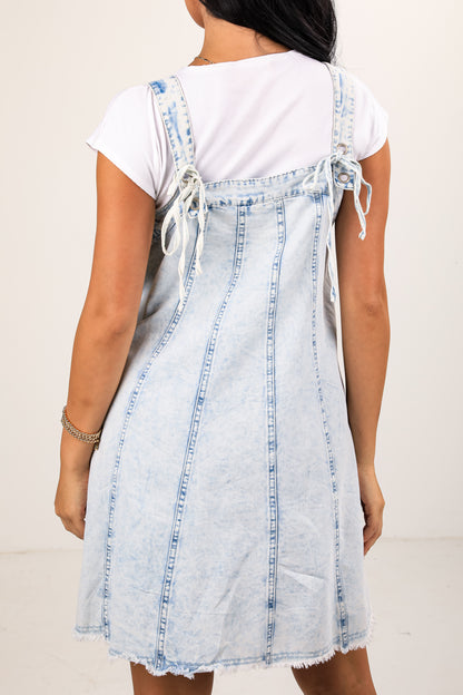Person wearing a denim dress over a white shirt against a plain background