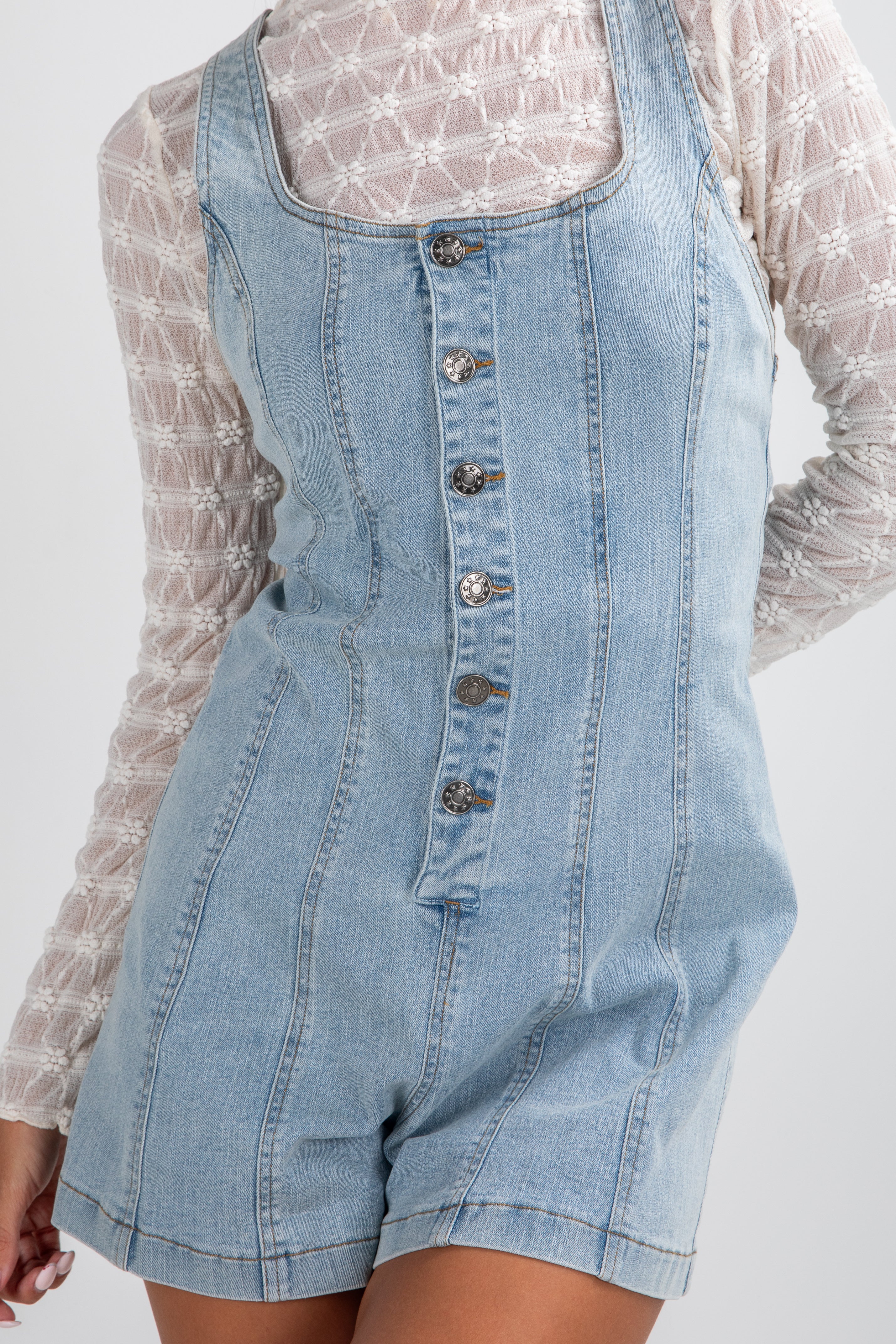 Denim overall shorts with a white lace top on a plain background