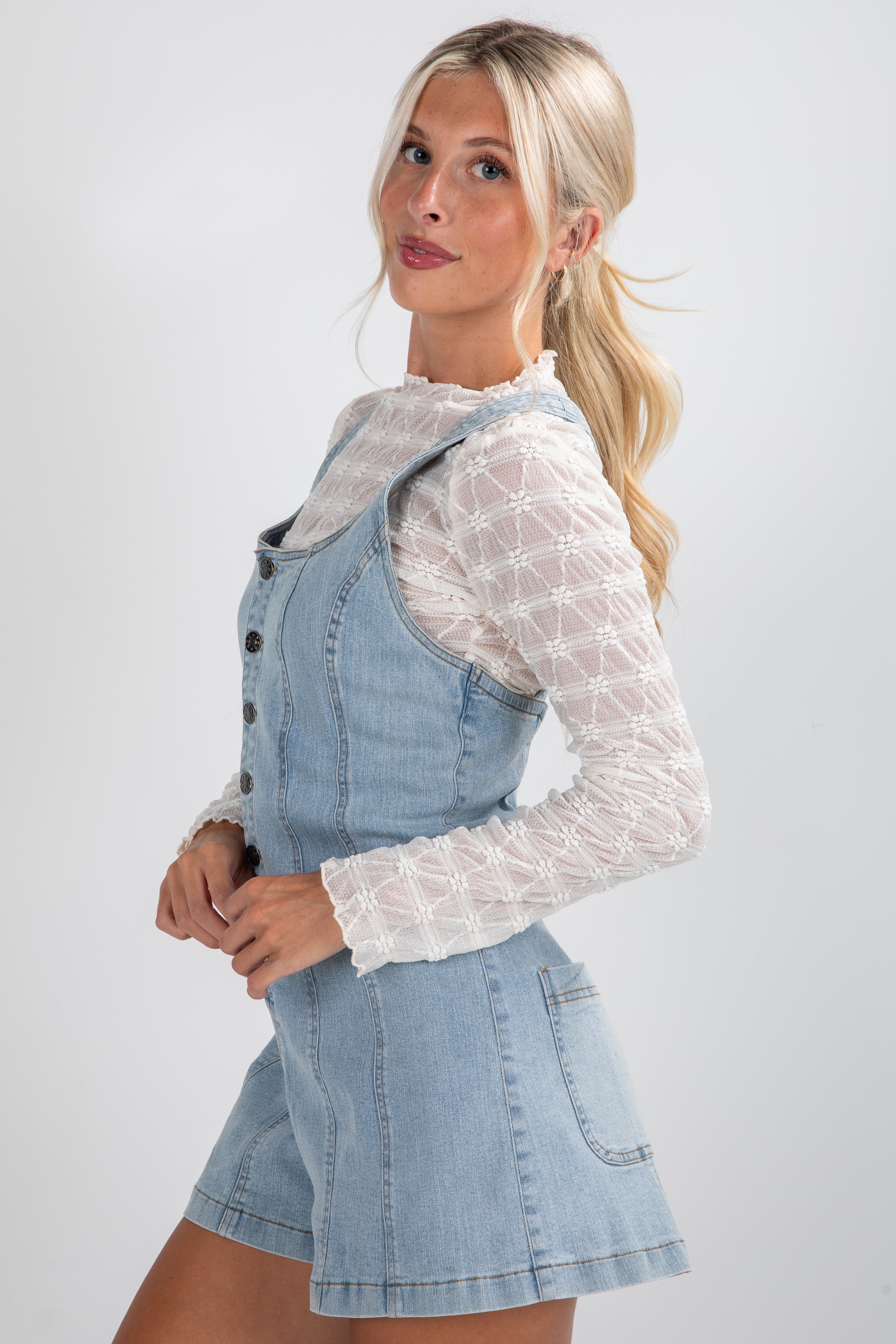 Woman wearing a denim dress over a white lace top on a light gray background